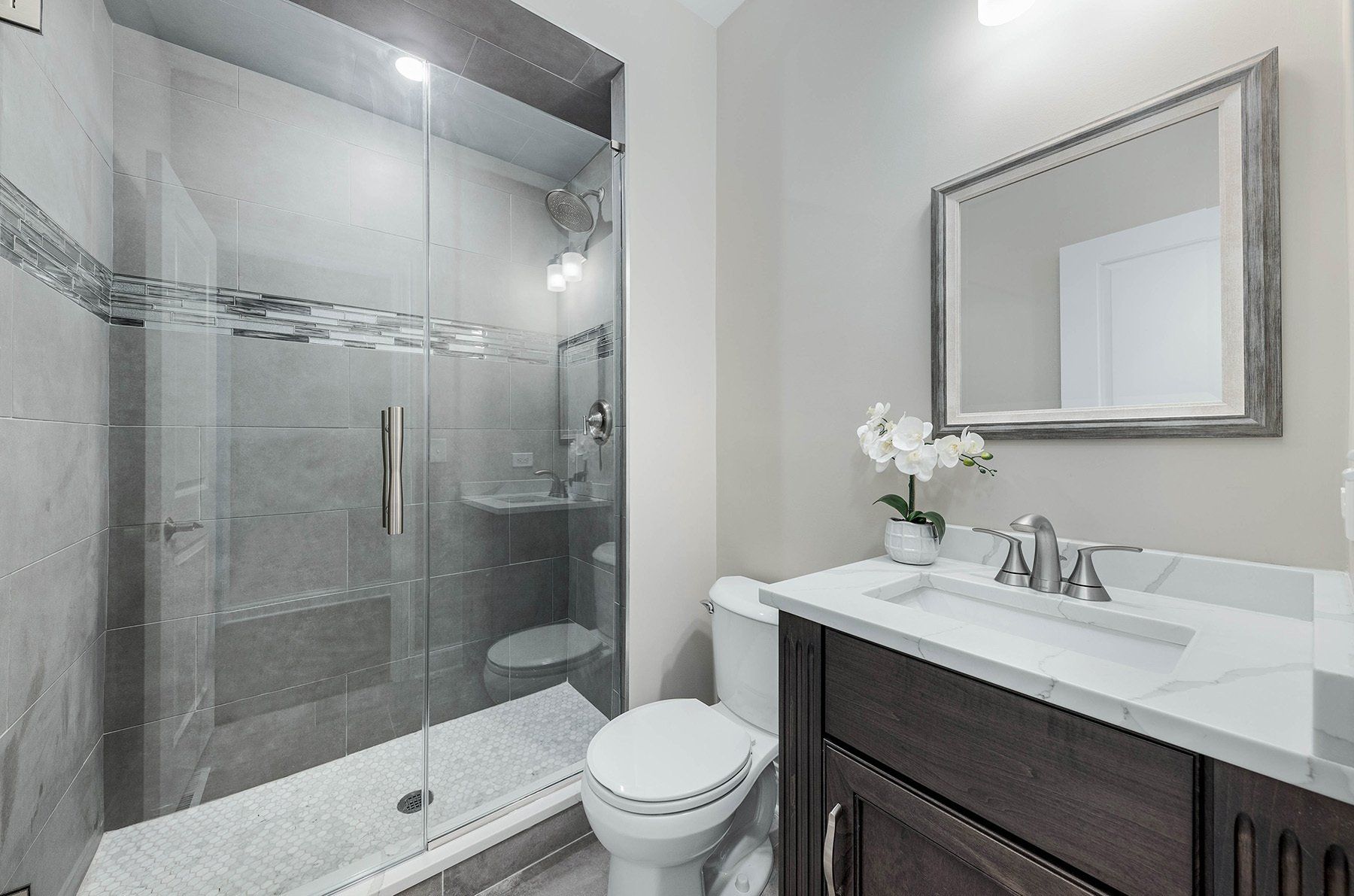 A bathroom with a toilet , sink , mirror and walk in shower.
