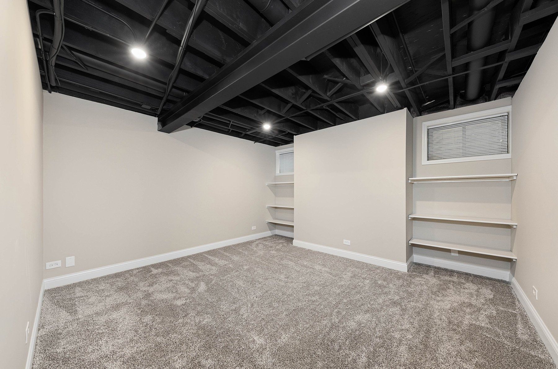 An empty basement with a black ceiling and carpet.