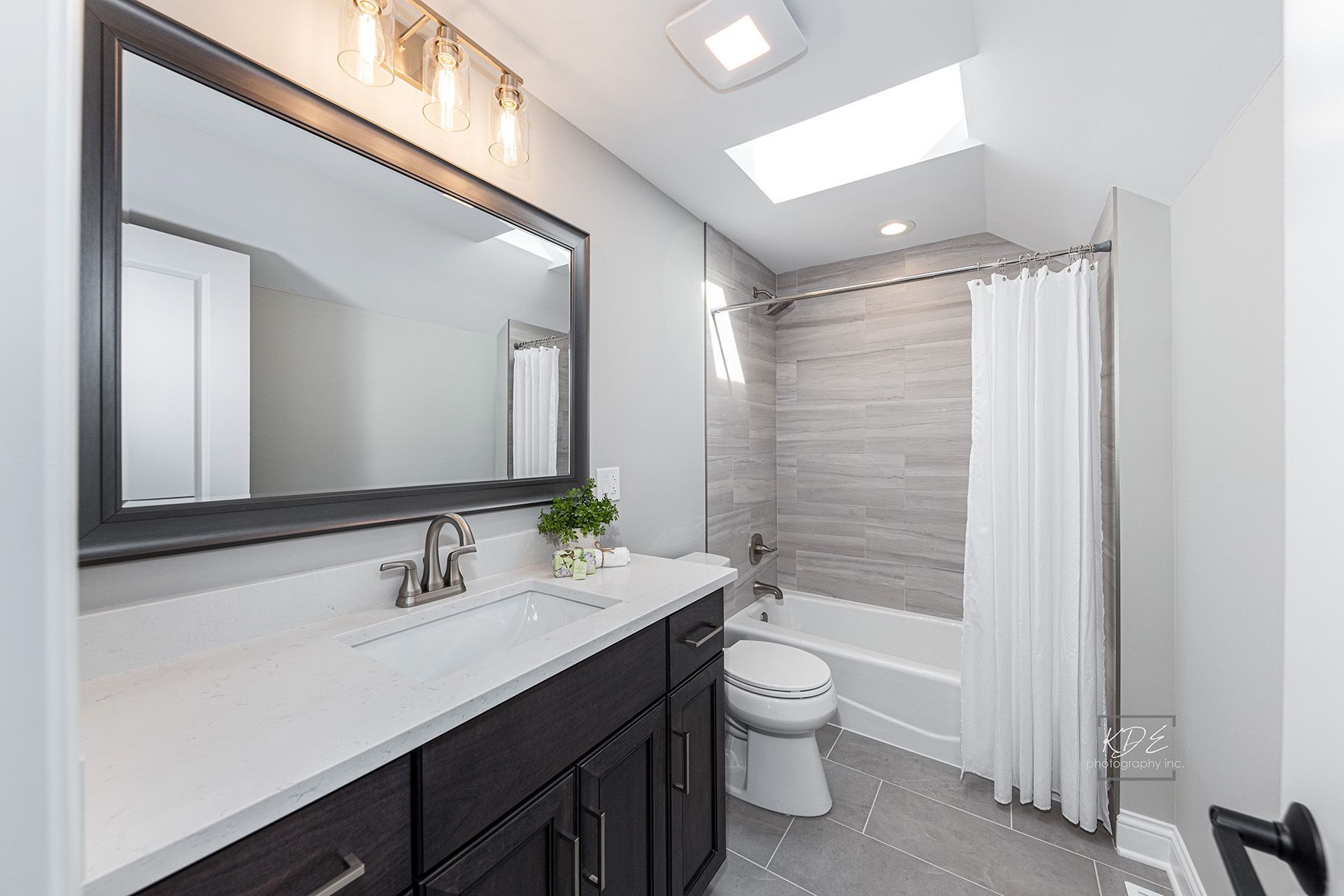 A bathroom with a sink , toilet , shower and mirror.