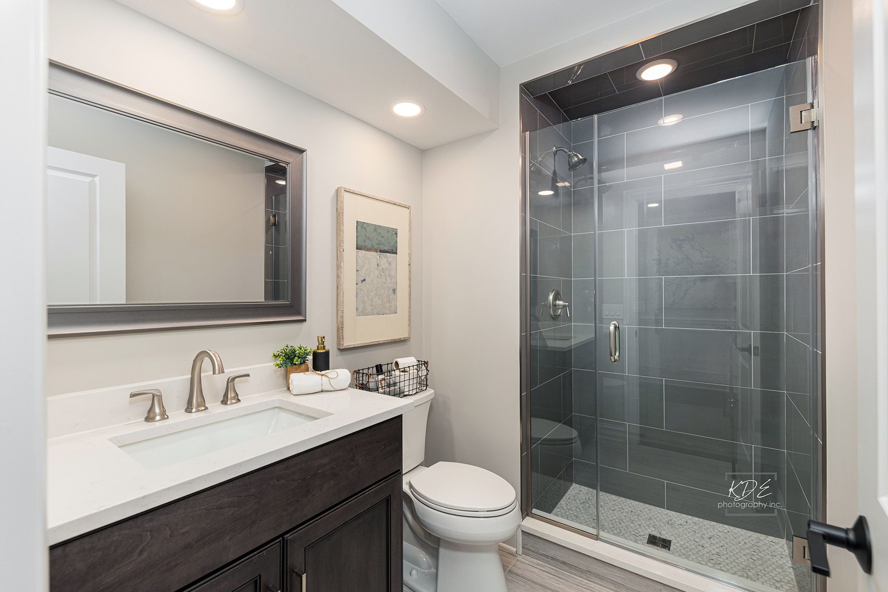 A bathroom with a toilet , sink , mirror and walk in shower.