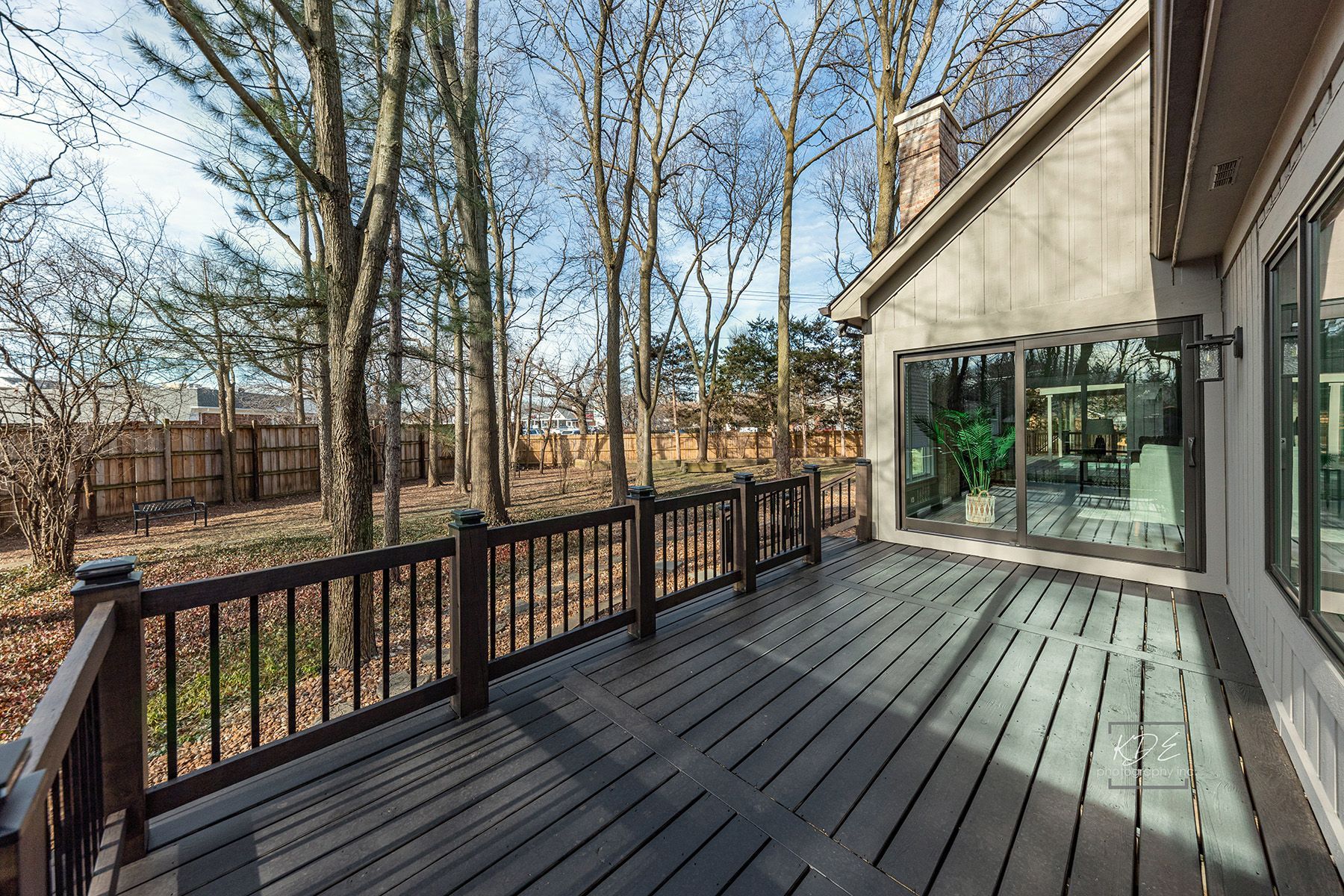A large deck with a railing and sliding glass doors surrounded by trees.