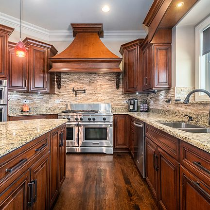 A kitchen with wooden cabinets , granite counter tops , stainless steel appliances and a stove.