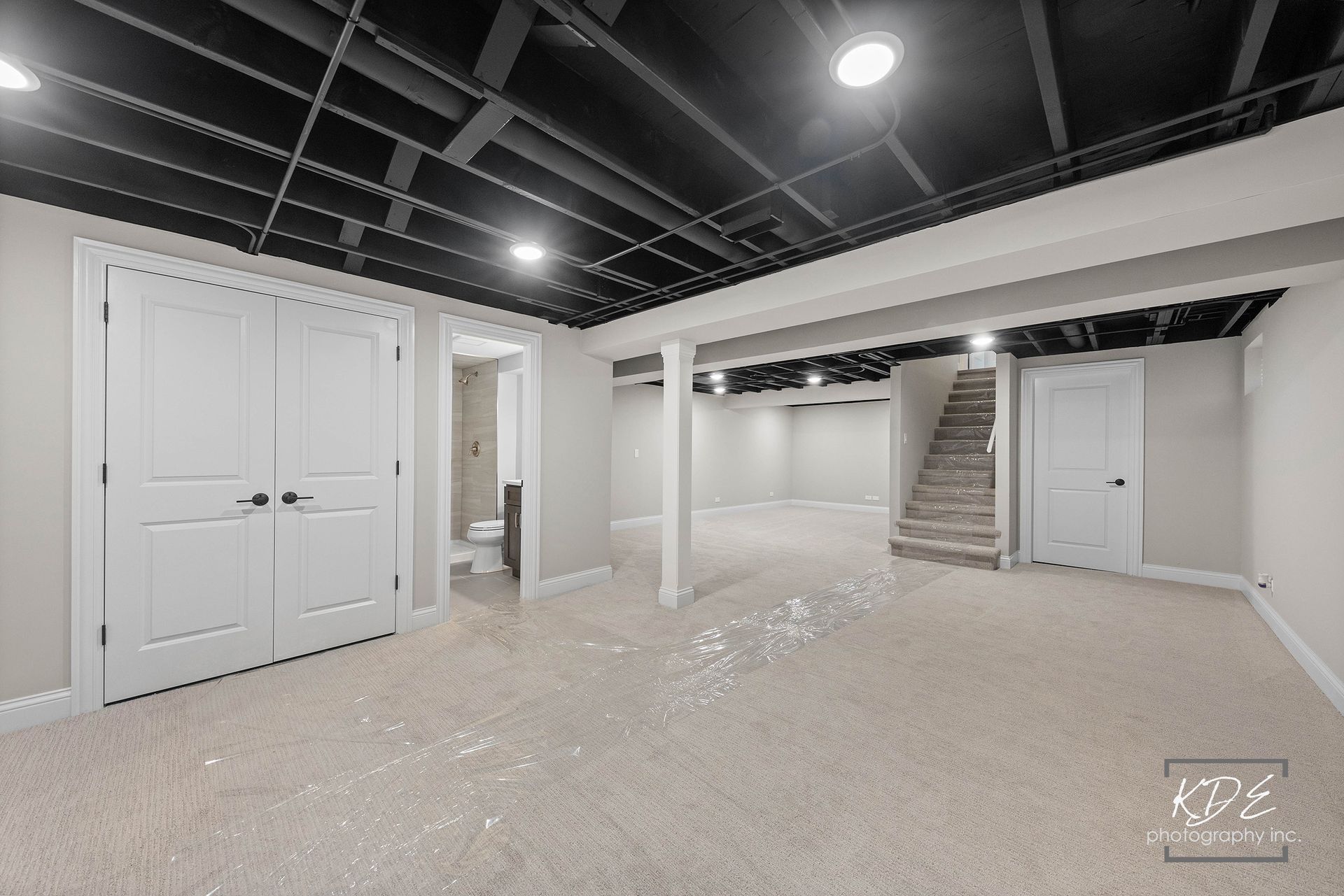 An empty basement with a black ceiling and stairs.
