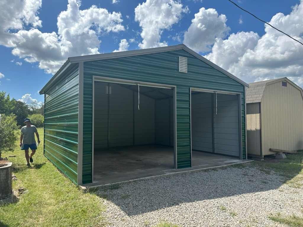 Green metal storage shed with open front doors on a gravel lot under a partly cloudy sky