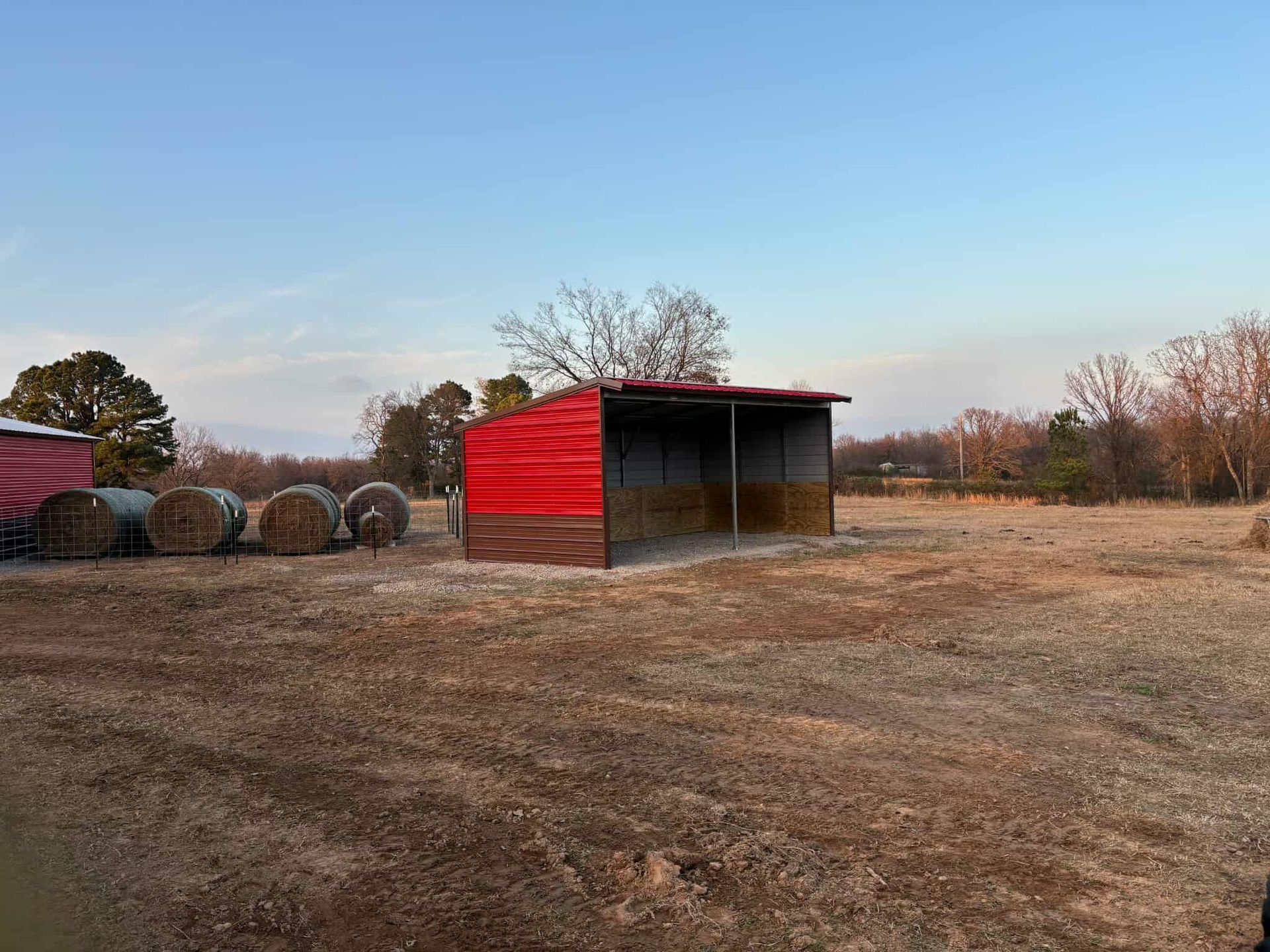 Red-roofed animal shelter in a dry, open field under a clear blue sky.