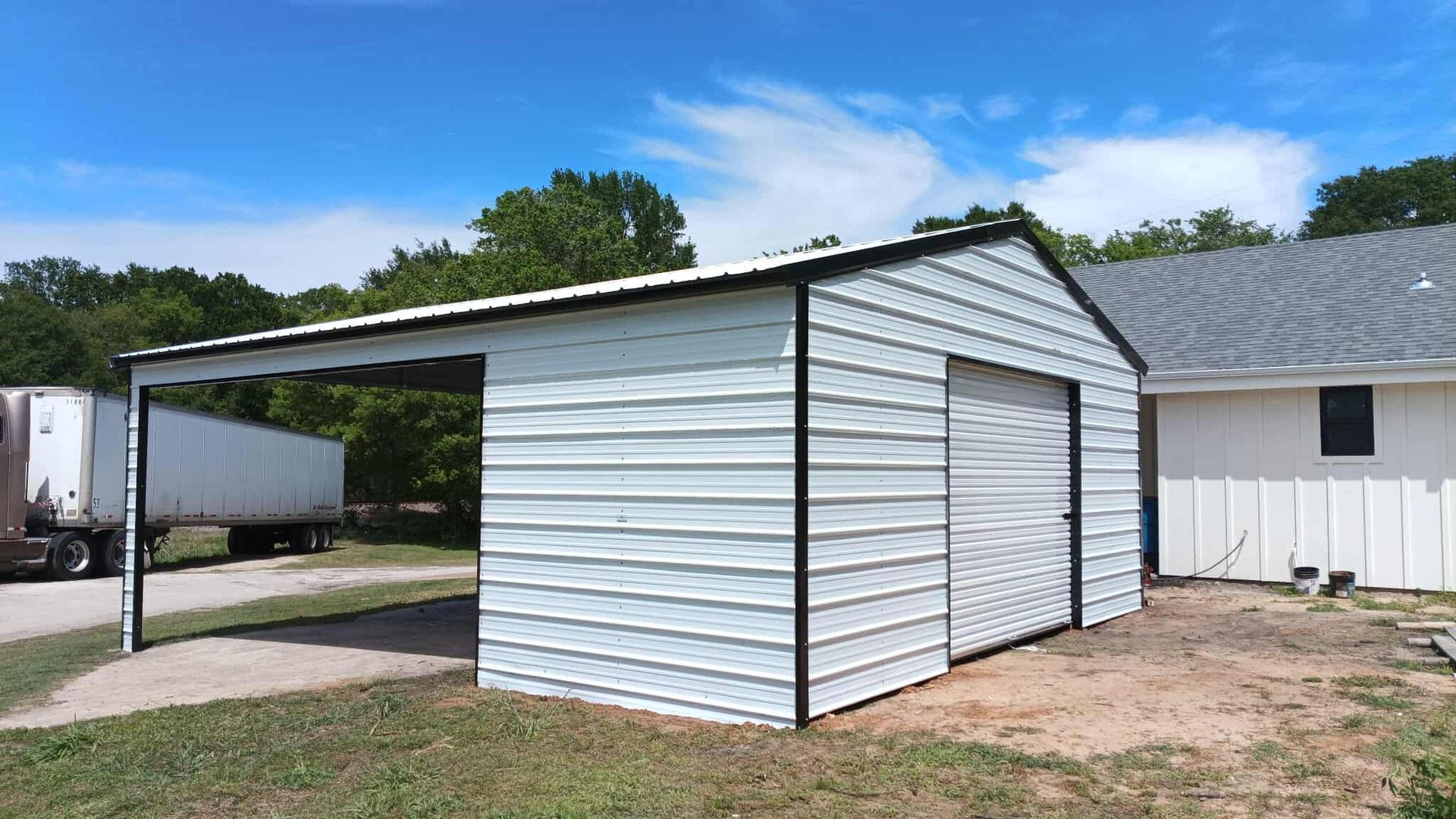 White metal carport attached to a small shed beside a house on a grassy lot.