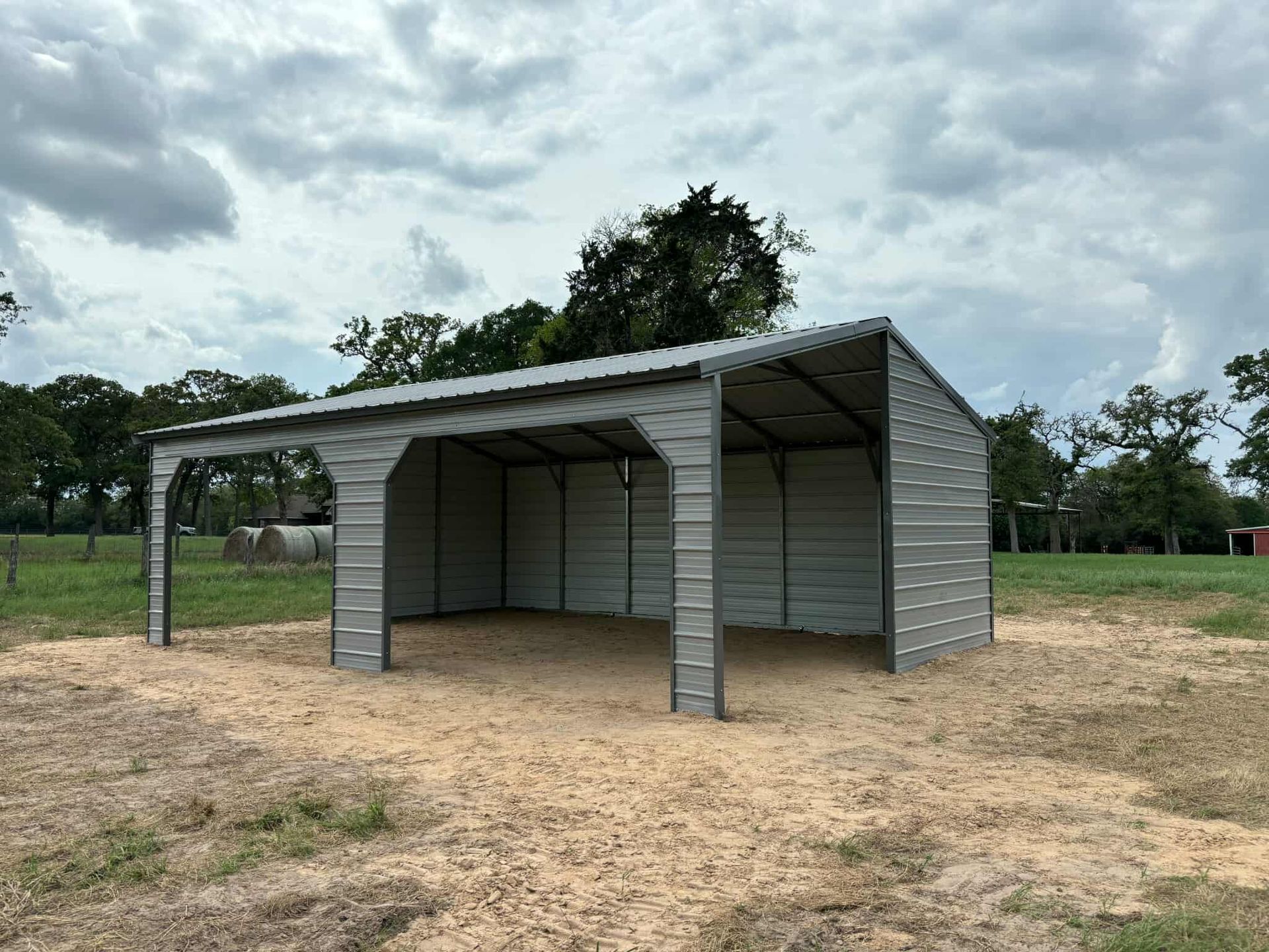 Open-sided gray metal shed in a dry field under a cloudy sky