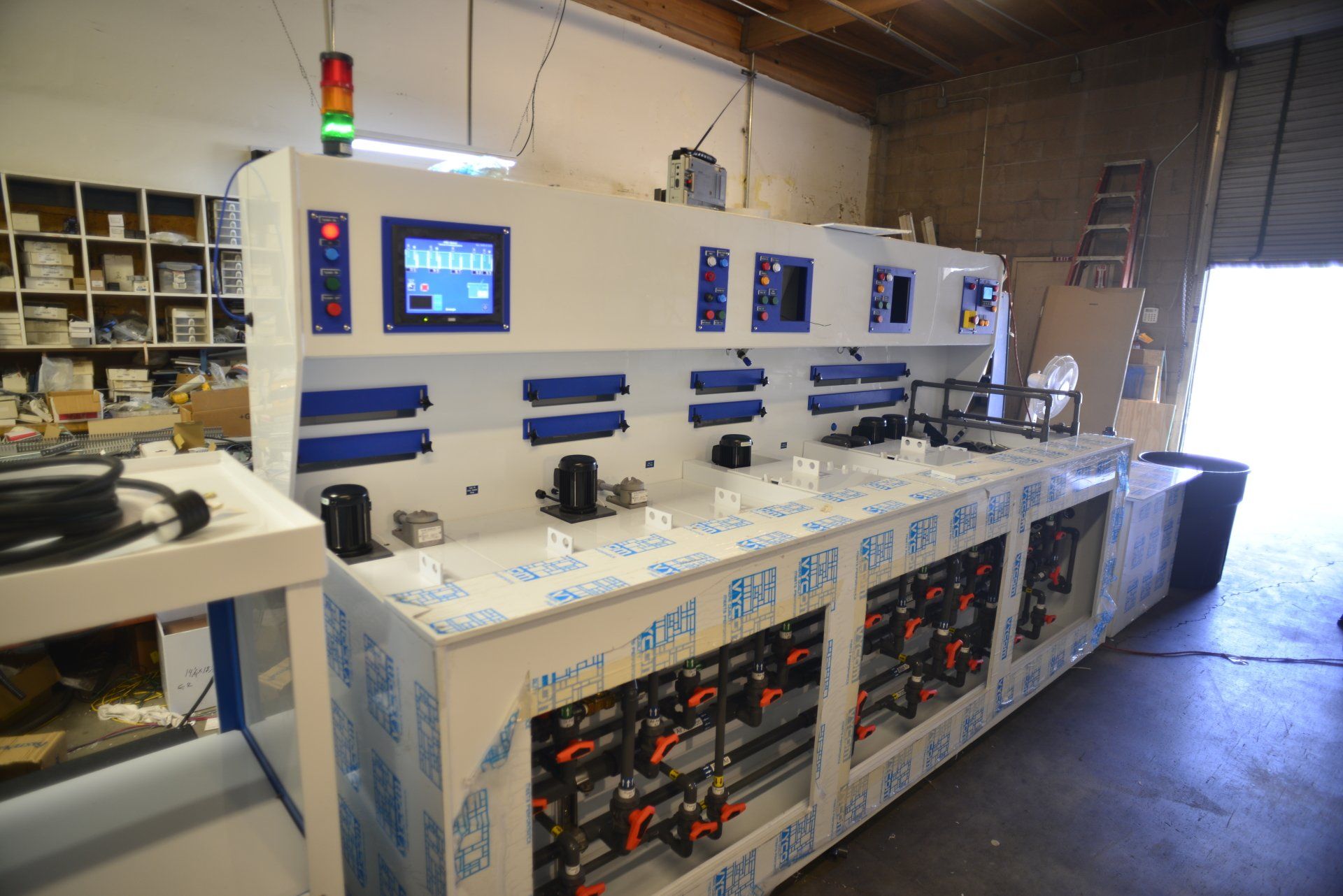 A large machine is sitting in a warehouse with a green light hanging from the ceiling.