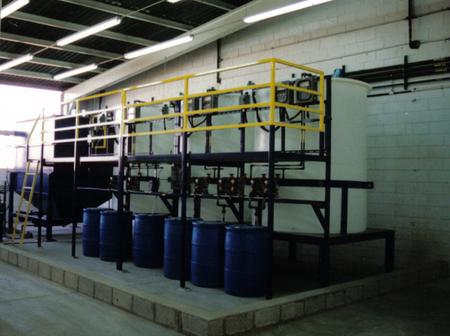 Blue barrels are lined up in a warehouse with a yellow railing