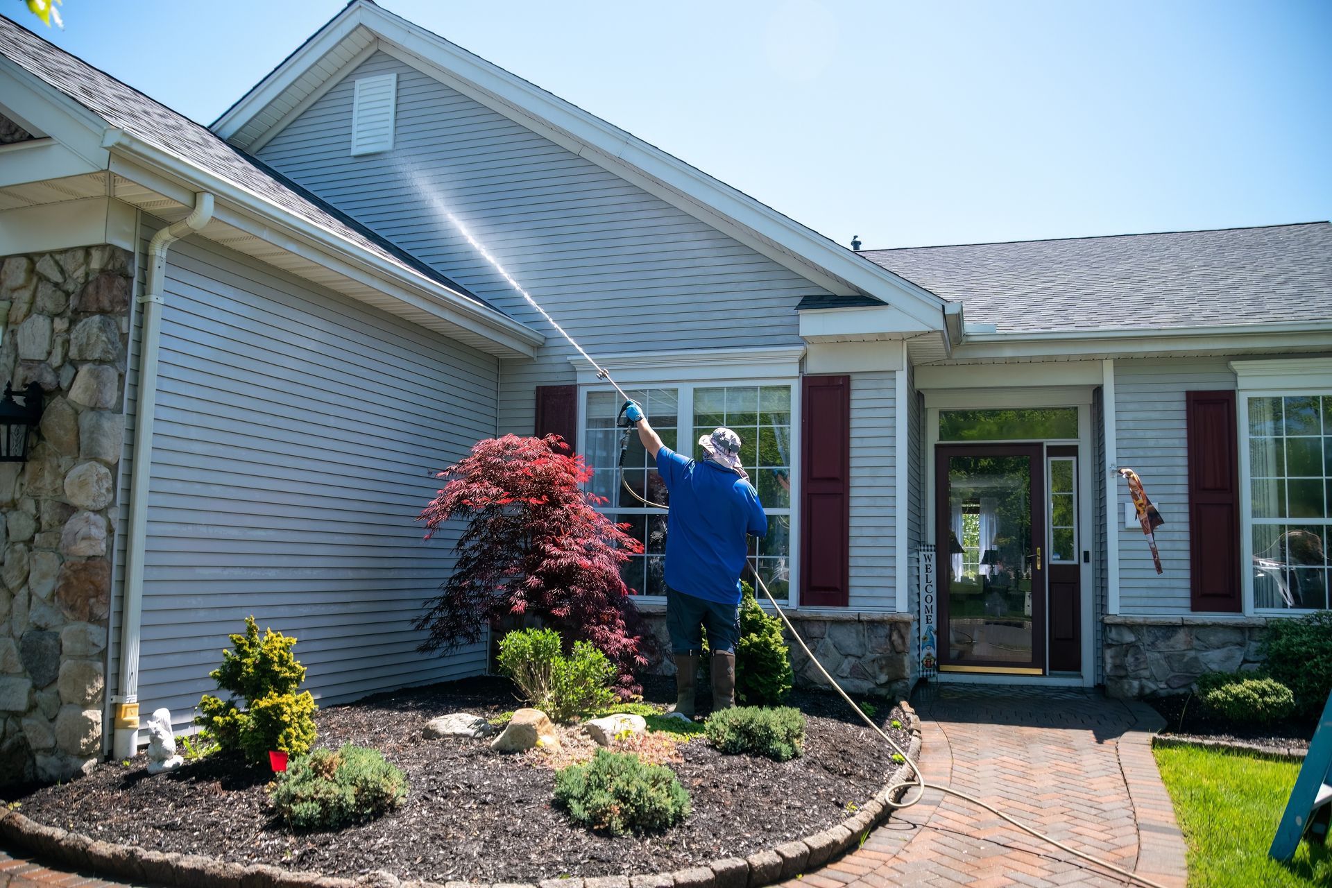 A caucasian man with a latex holding water sprayer wand power washing the siding of a house