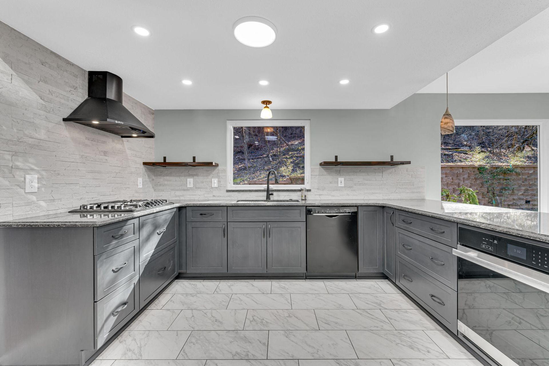 A kitchen with gray cabinets , granite counter tops , stainless steel appliances and a window.