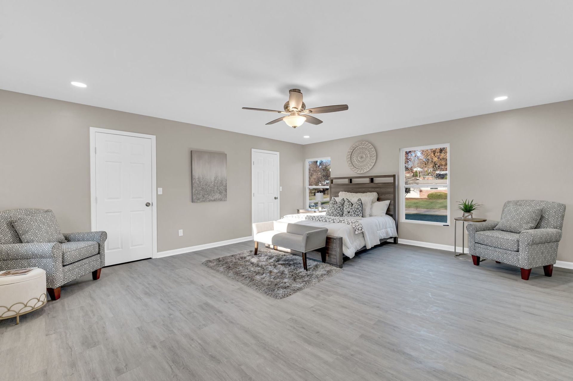 A large bedroom with a bed , chairs , and a ceiling fan.