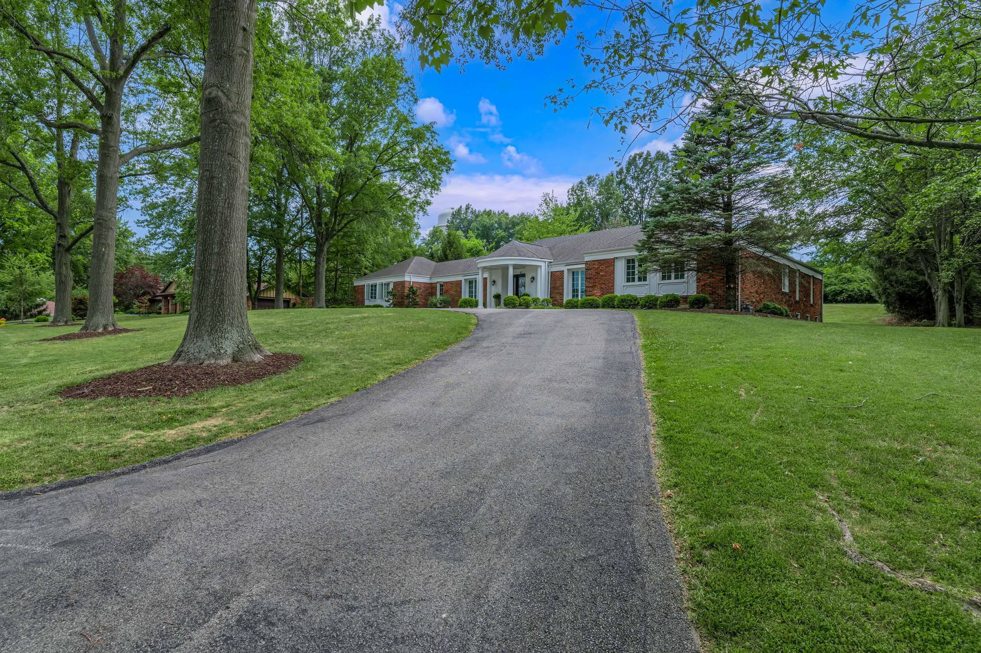 A driveway leading to a house surrounded by trees and grass.