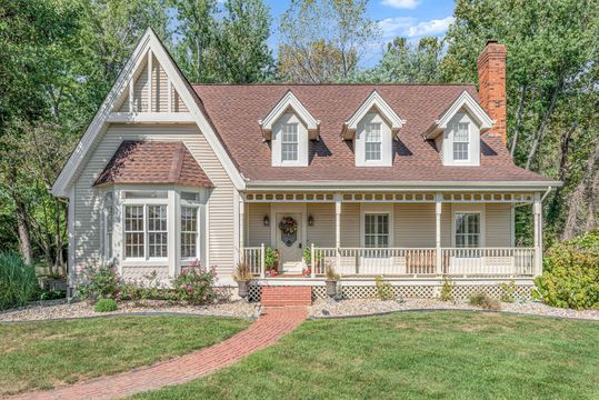 A small white house with a porch and a brick walkway leading to it.