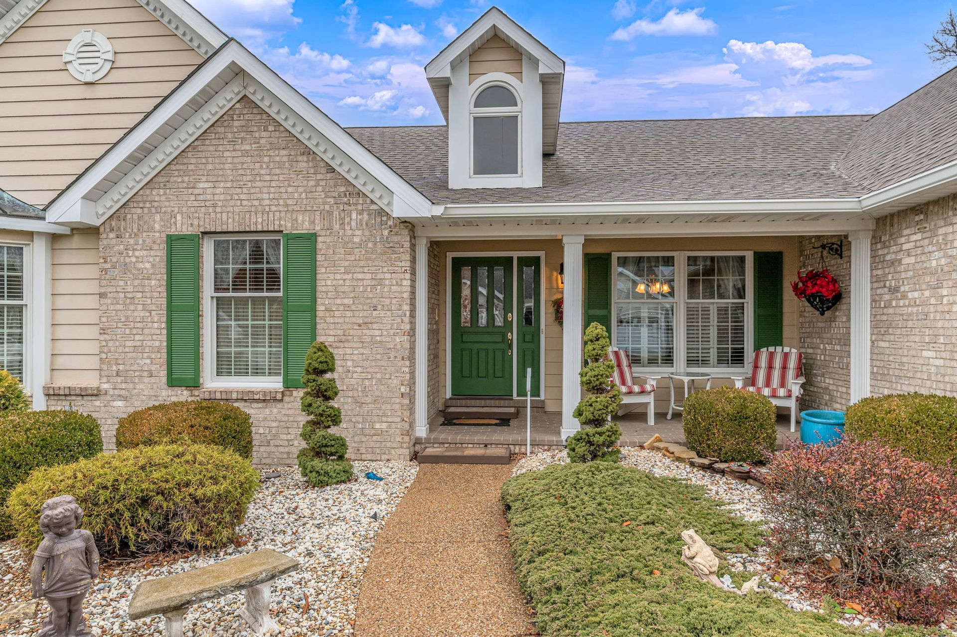 The front of a brick house with a green door and green shutters.