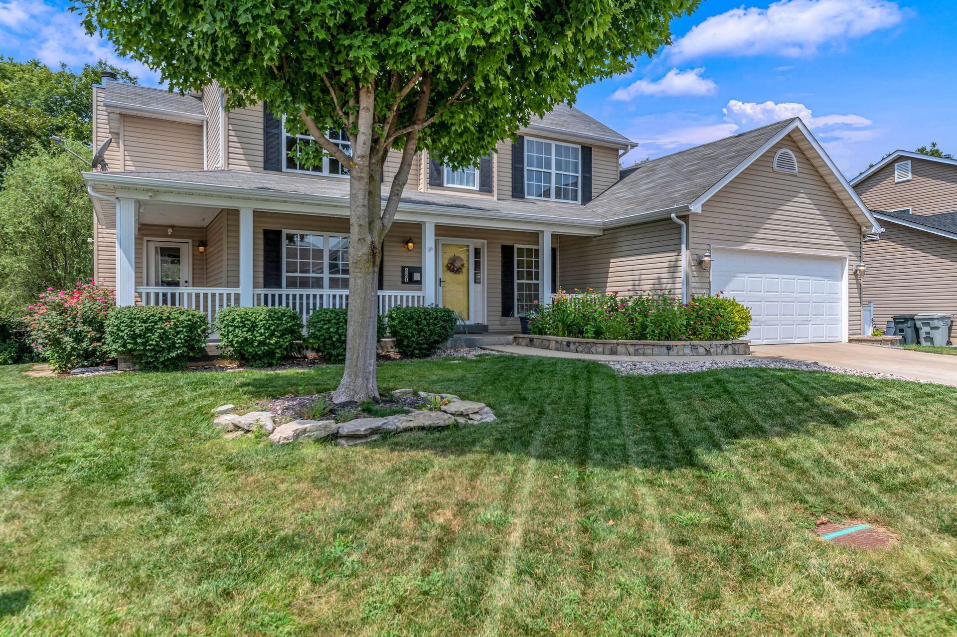 A large house with a large porch and a tree in front of it.