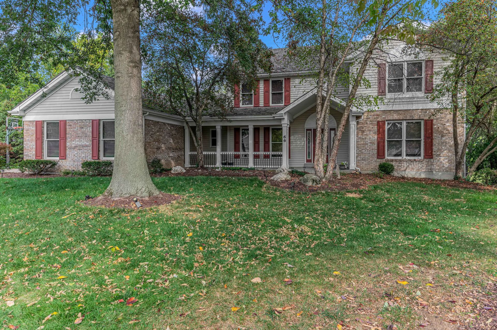A large white house with red shutters and a large tree in front of it.