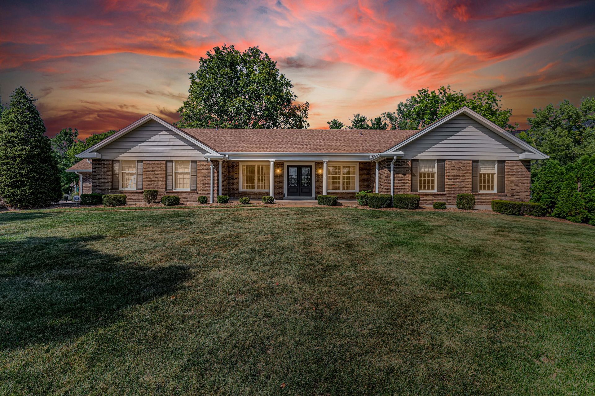 A large brick house with a large lawn in front of it and a sunset in the background.