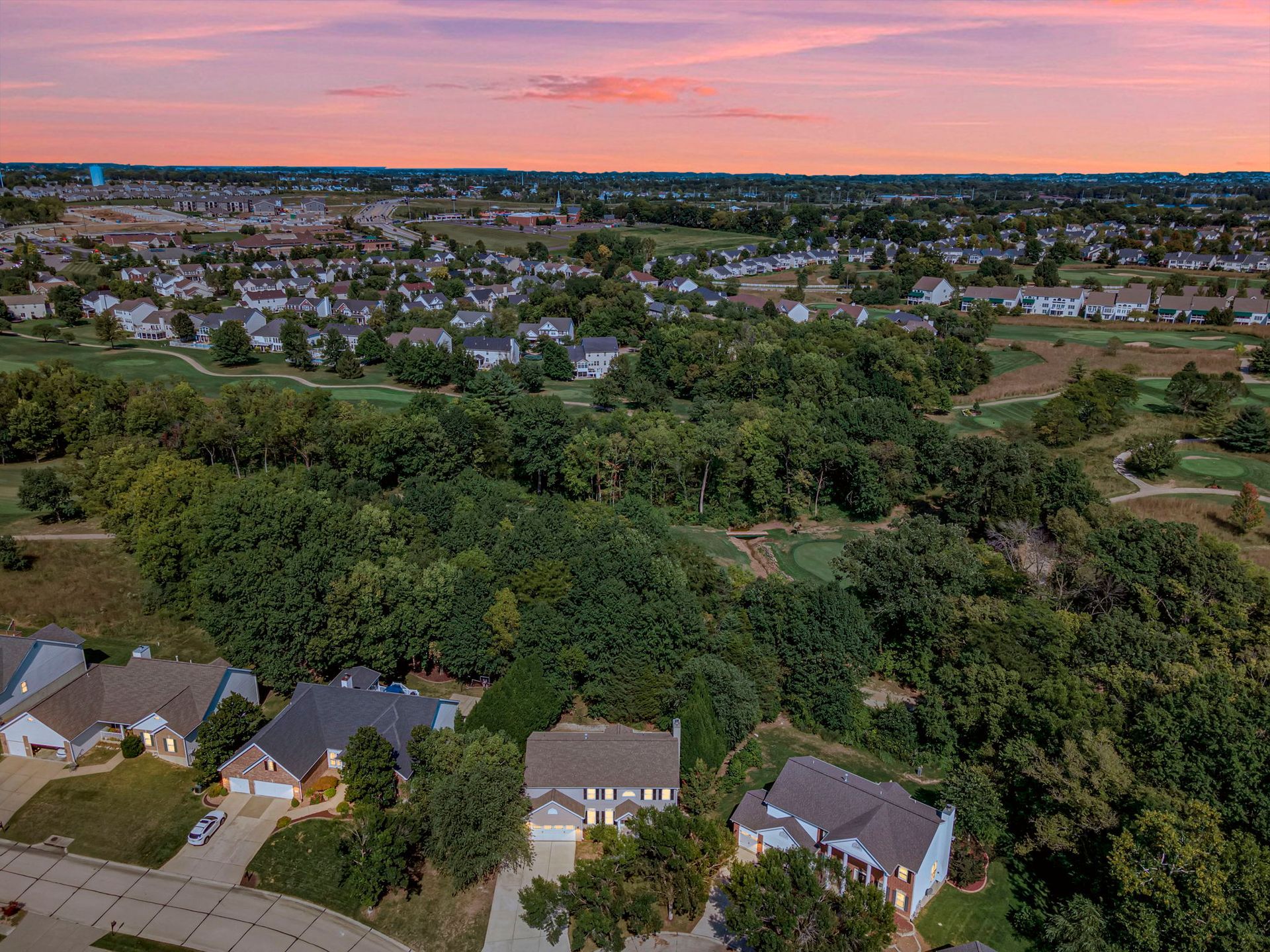 An aerial view of a residential area with houses and trees at sunset.