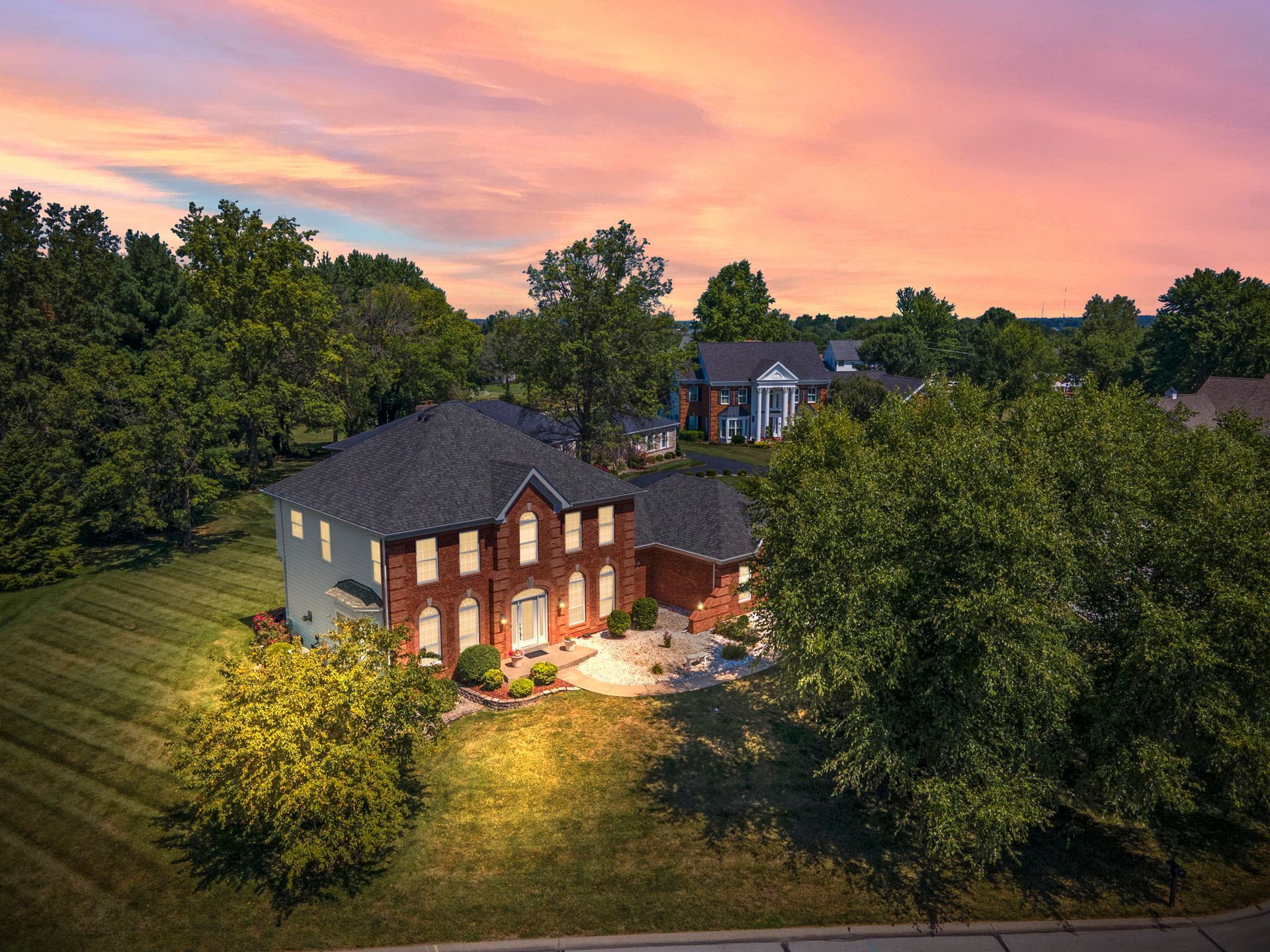 An aerial view of a large brick house surrounded by trees at sunset.