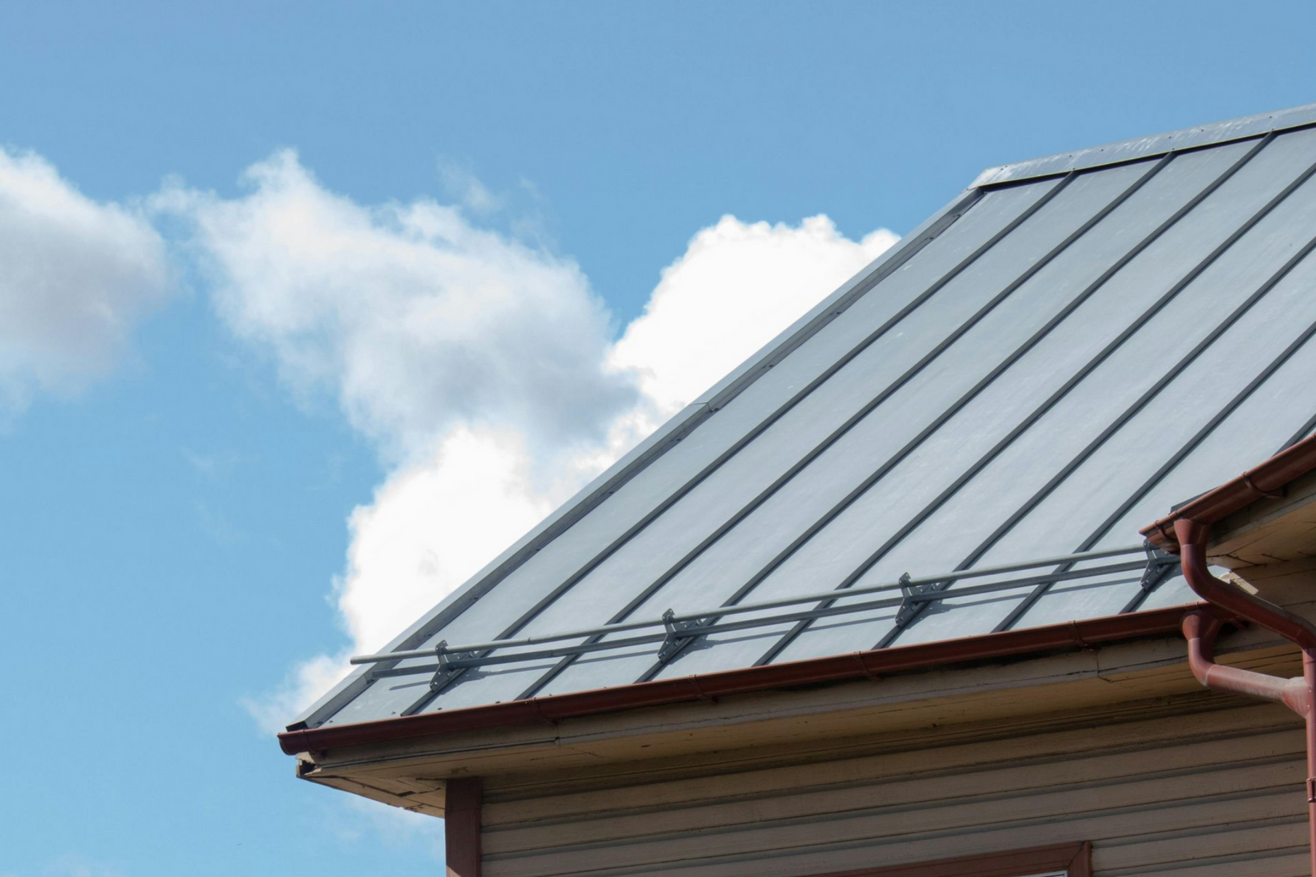Metal roof with gray panels under a blue sky and clouds