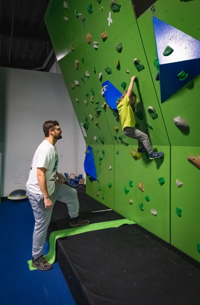 Young boy climbing wall with instructor looking