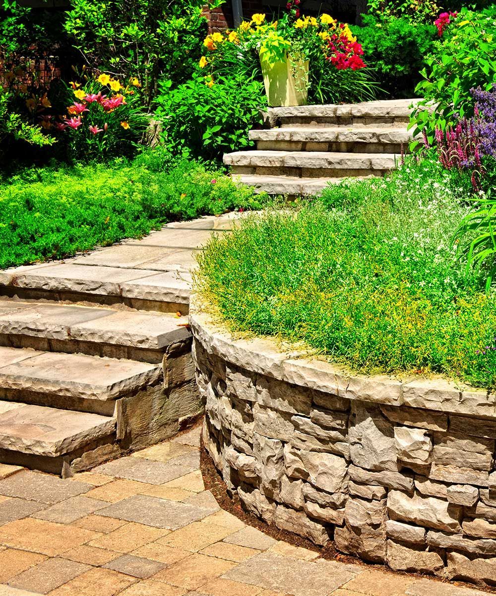 A stone walkway with stairs leading up to a stone wall in a garden.