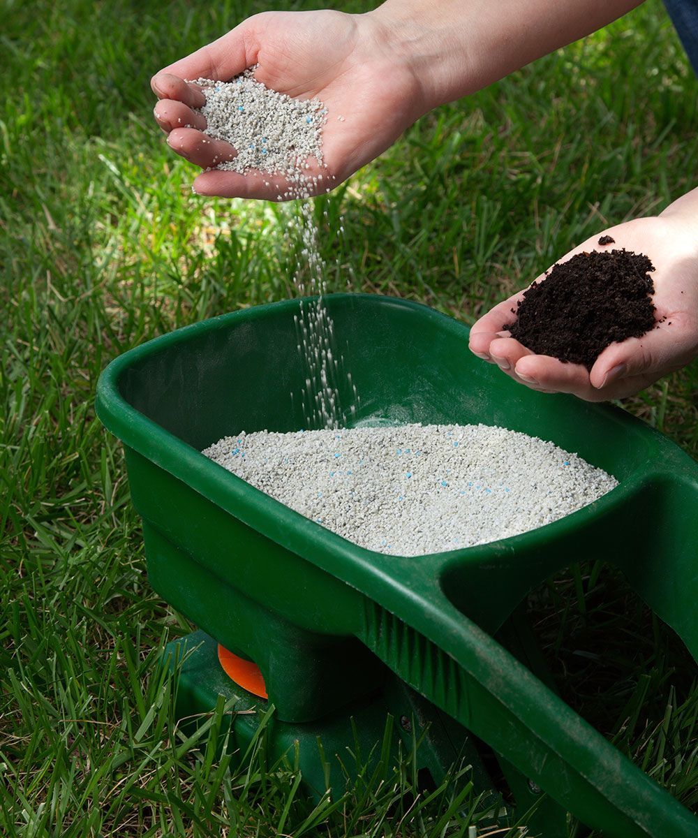 A person is pouring fertilizer into a green wheelbarrow.