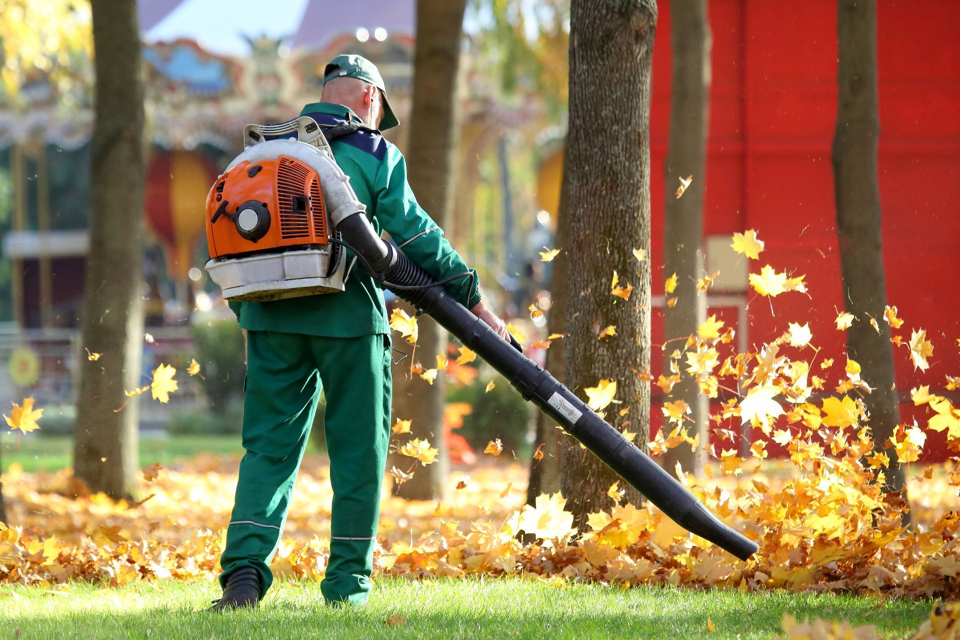 A man is blowing leaves in a park with a backpack blower.