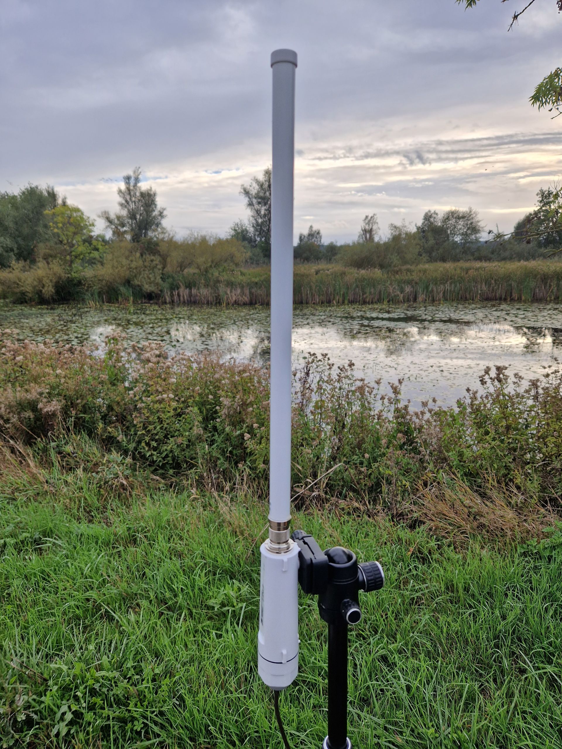 Een witte antenne zit in het gras vlakbij een watermassa.