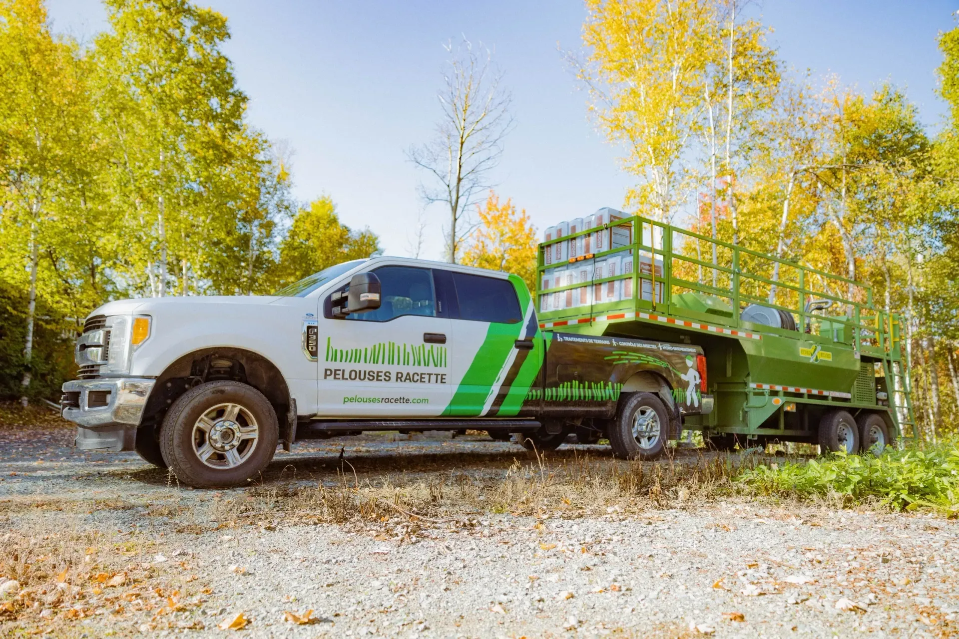 Un camion vert et blanc auquel est attachée une remorque est garé sur une route de gravier.