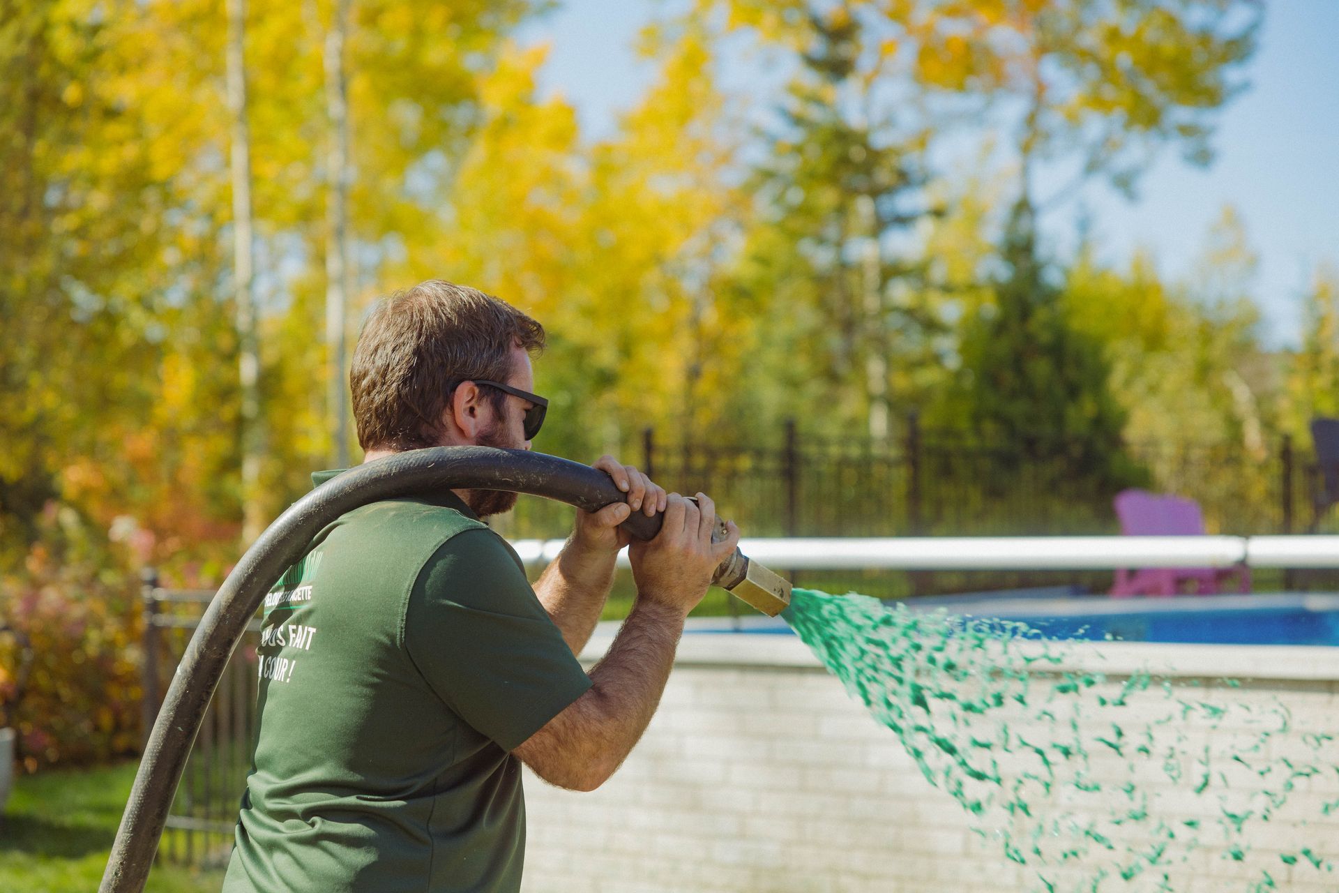 Un homme pulvérise de l’eau à partir d’un tuyau dans une piscine.