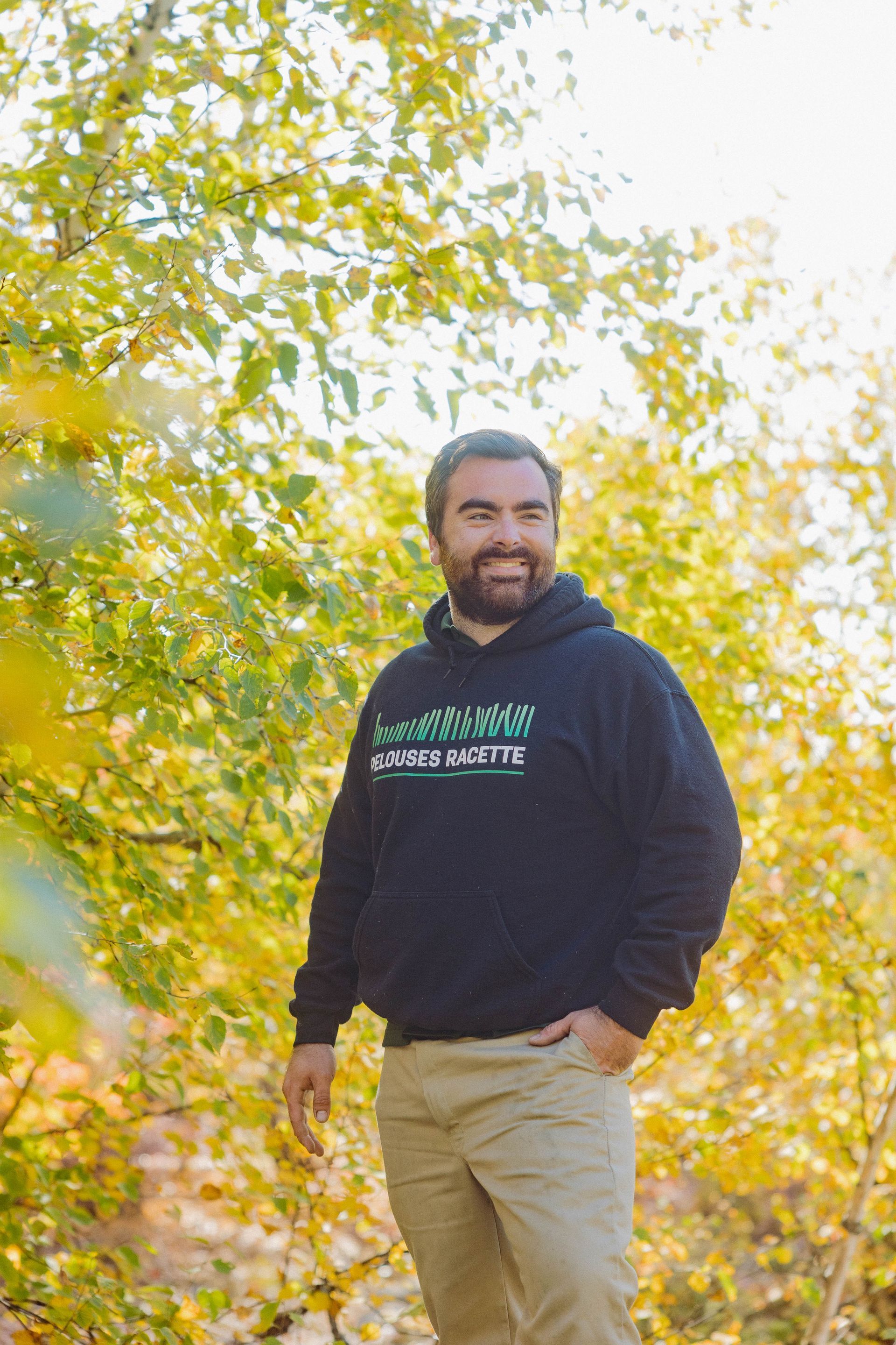 Un homme barbu porte un sweat à capuche noir et un pantalon kaki.