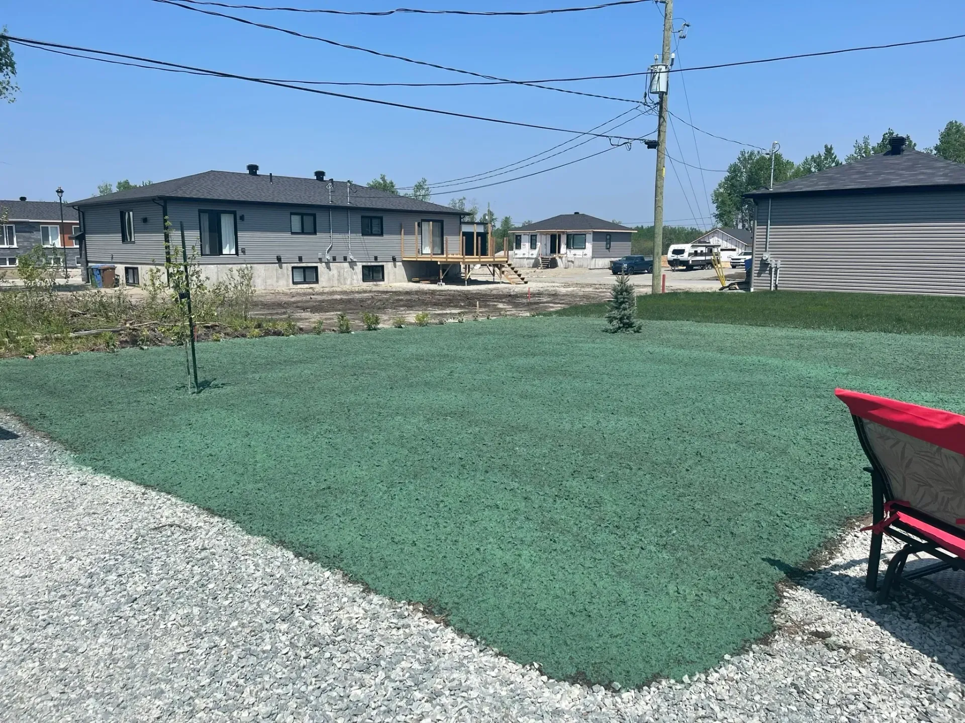 Une pelouse verte avec une brouette au premier plan et des maisons en arrière-plan.