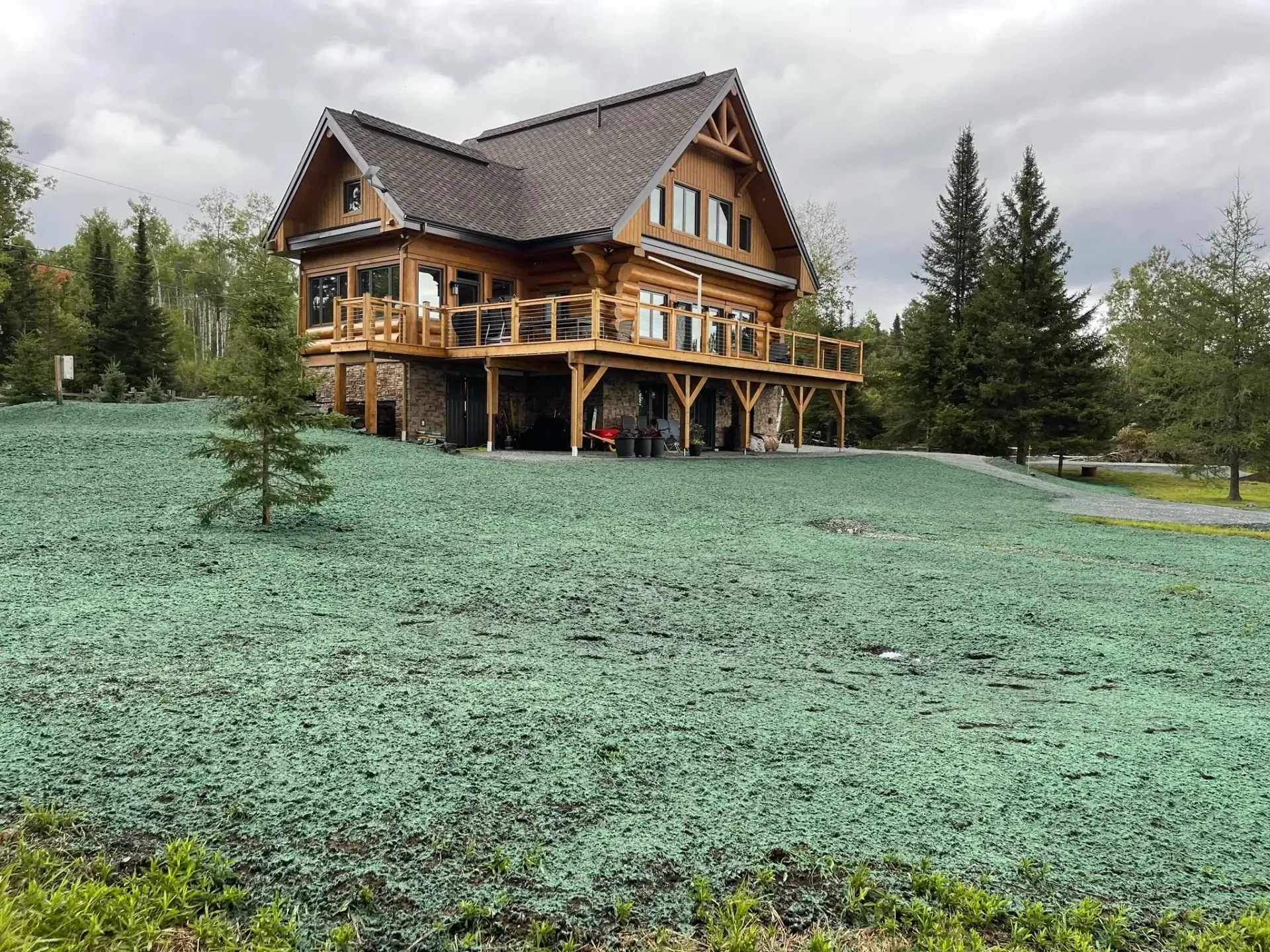 Une grande maison en bois se trouve au sommet d’une colline herbeuse.