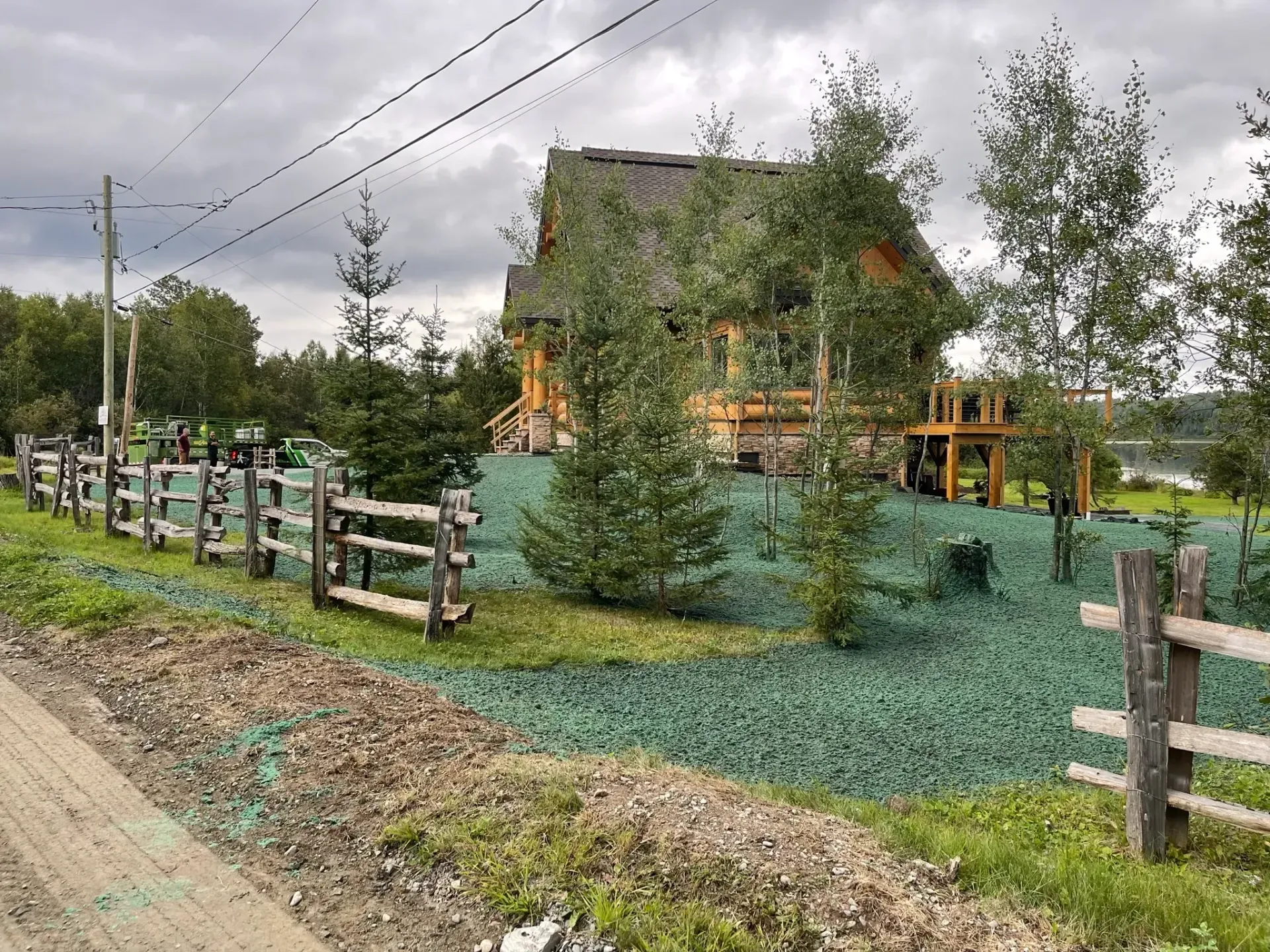 Une clôture en bois entoure un champ verdoyant avec une maison en arrière-plan.