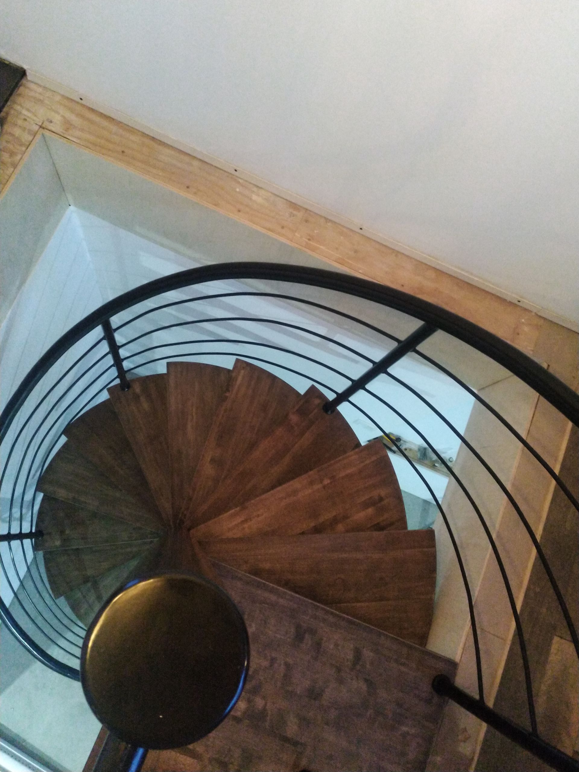 Escalier en colimaçon en bois avec rampe noire.