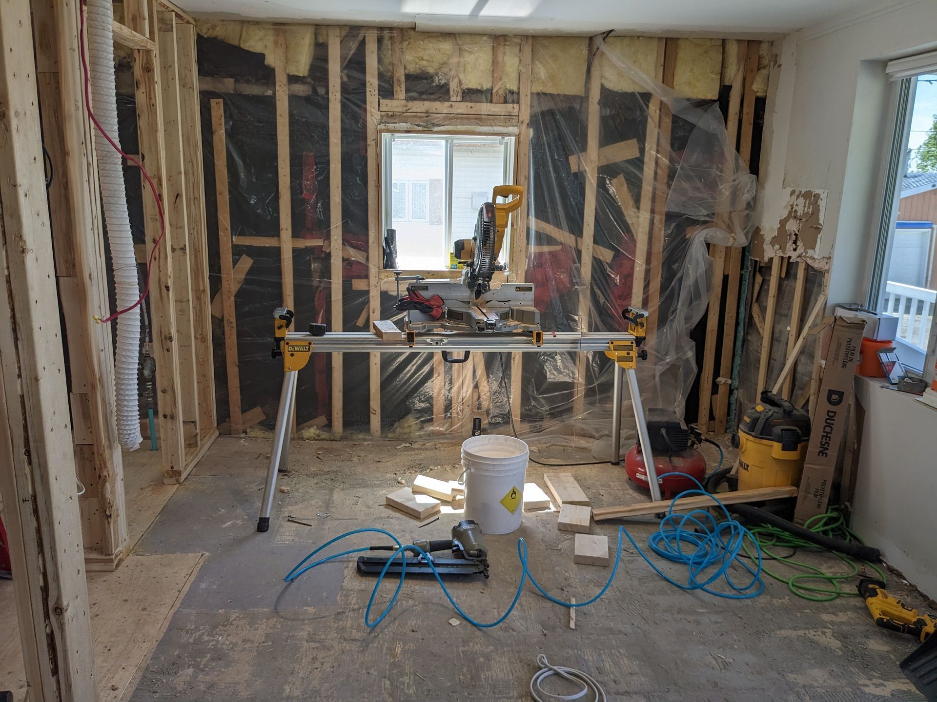 Chambre en construction; charpente en bois apparente, scie à onglet sur support, outils et débris.