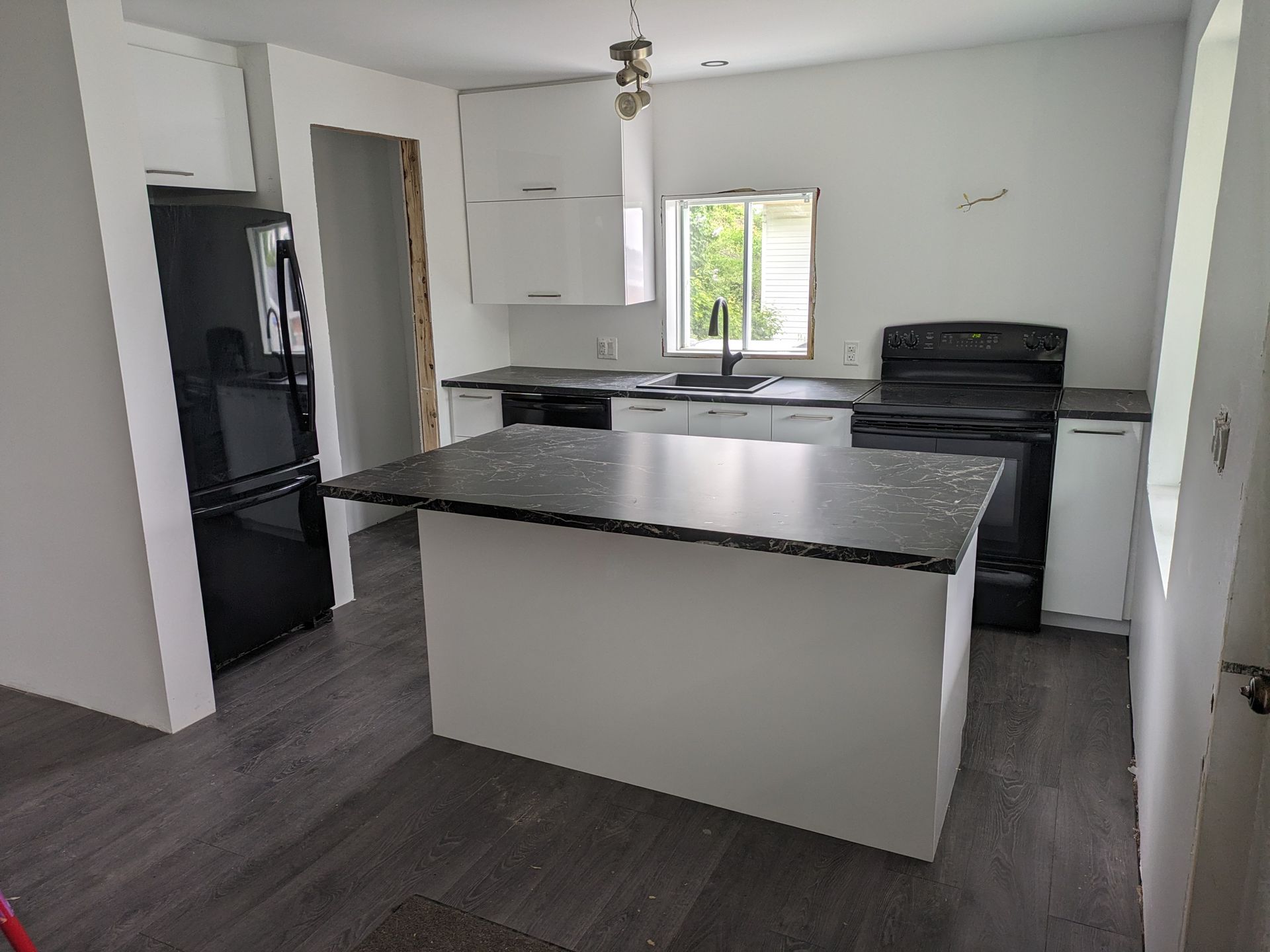 Cuisine moderne avec armoires blanches, électroménagers noirs, îlot et comptoirs foncés.