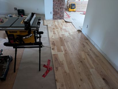 Pose de parquet en cours; table de scie à gauche, planches de bois disposées.