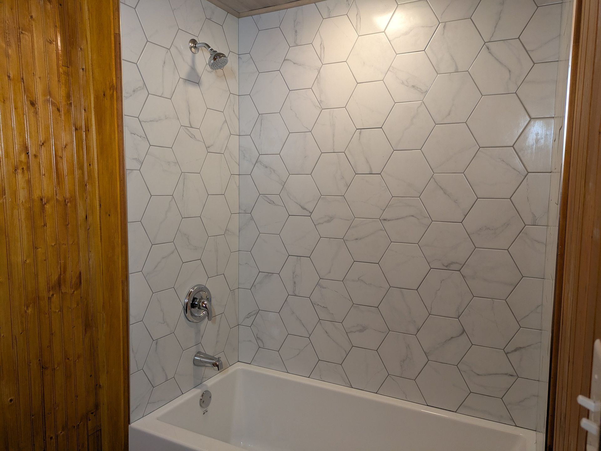 Salle de bain avec douche en carrelage hexagonal blanc et baignoire blanche.