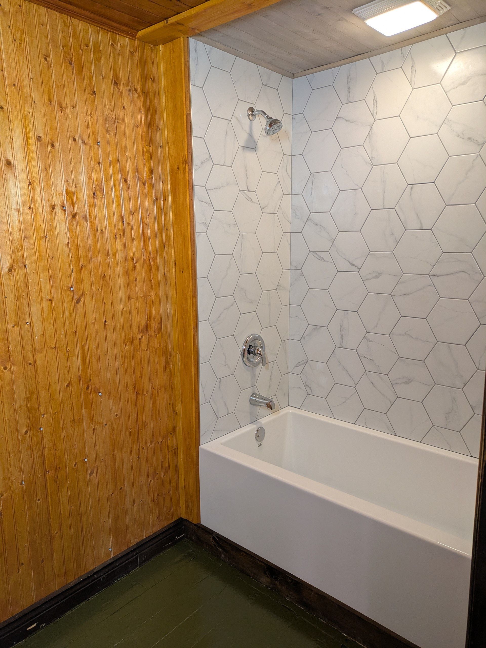 Salle de bain avec douche en carrelage hexagonal blanc, baignoire blanche et murs en boiseries.