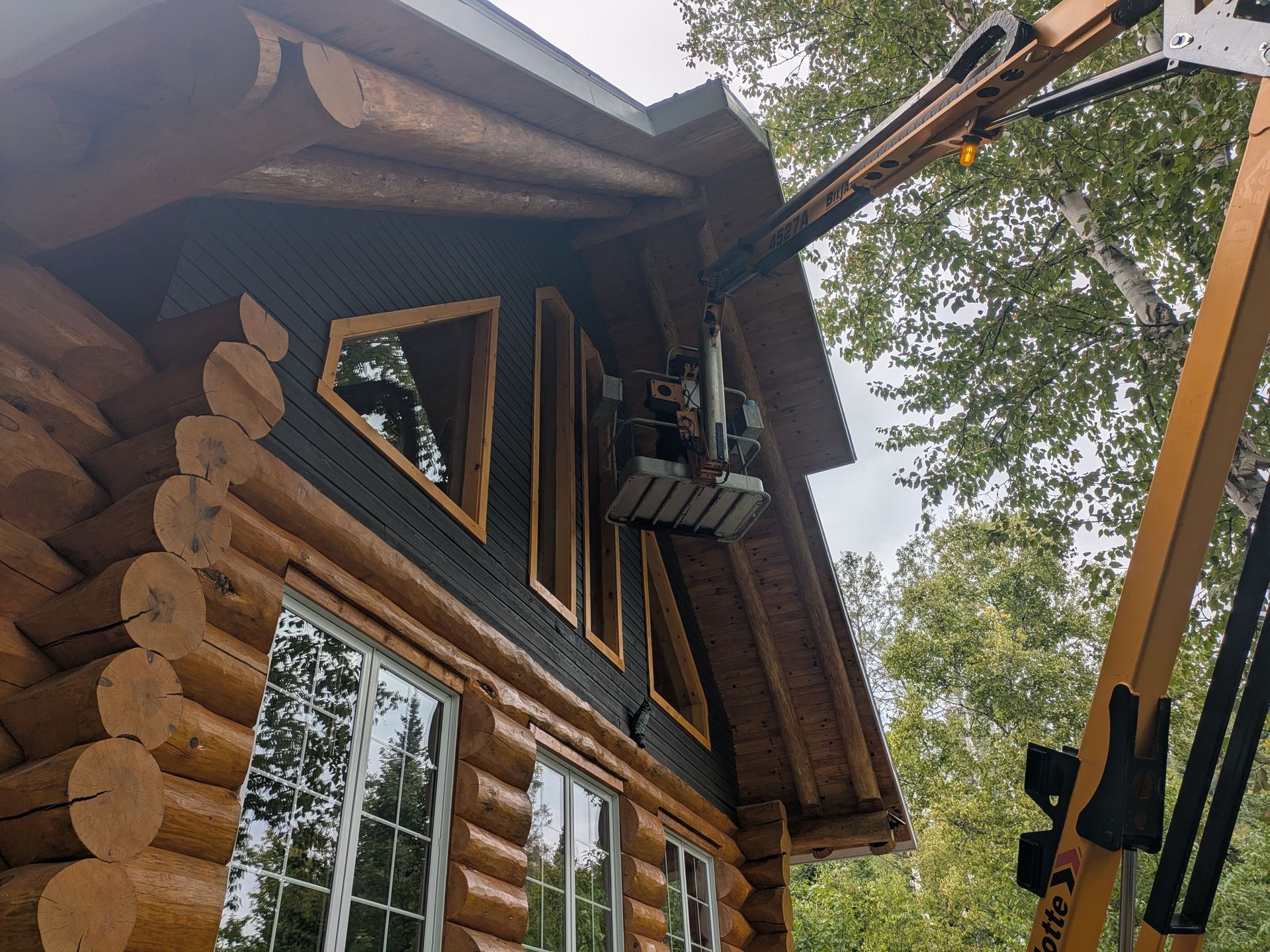 Cabane en rondins avec ascenseur ; un ouvrier peint les boiseries.