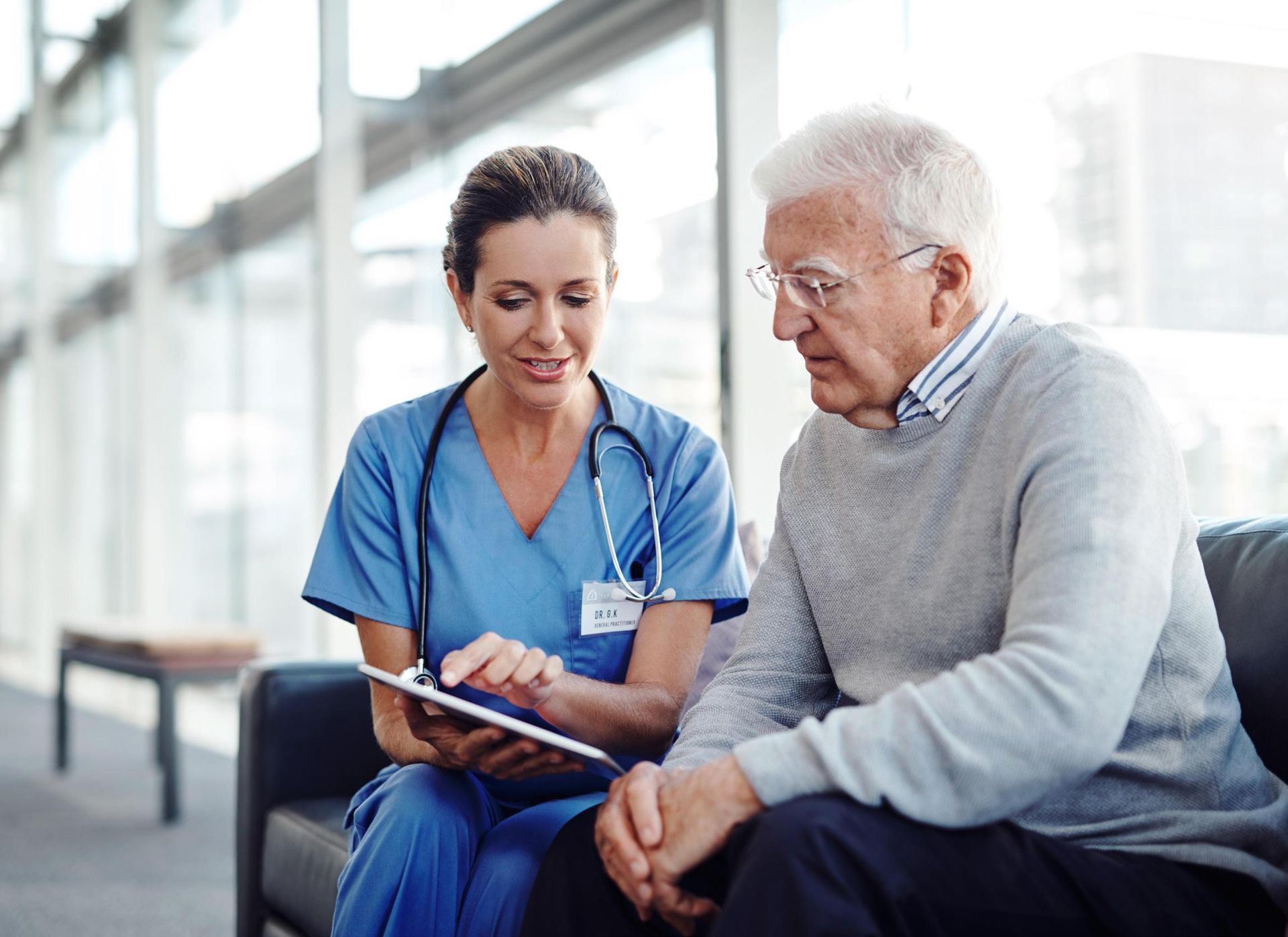A nurse is talking to an elderly man while looking at a tablet.
