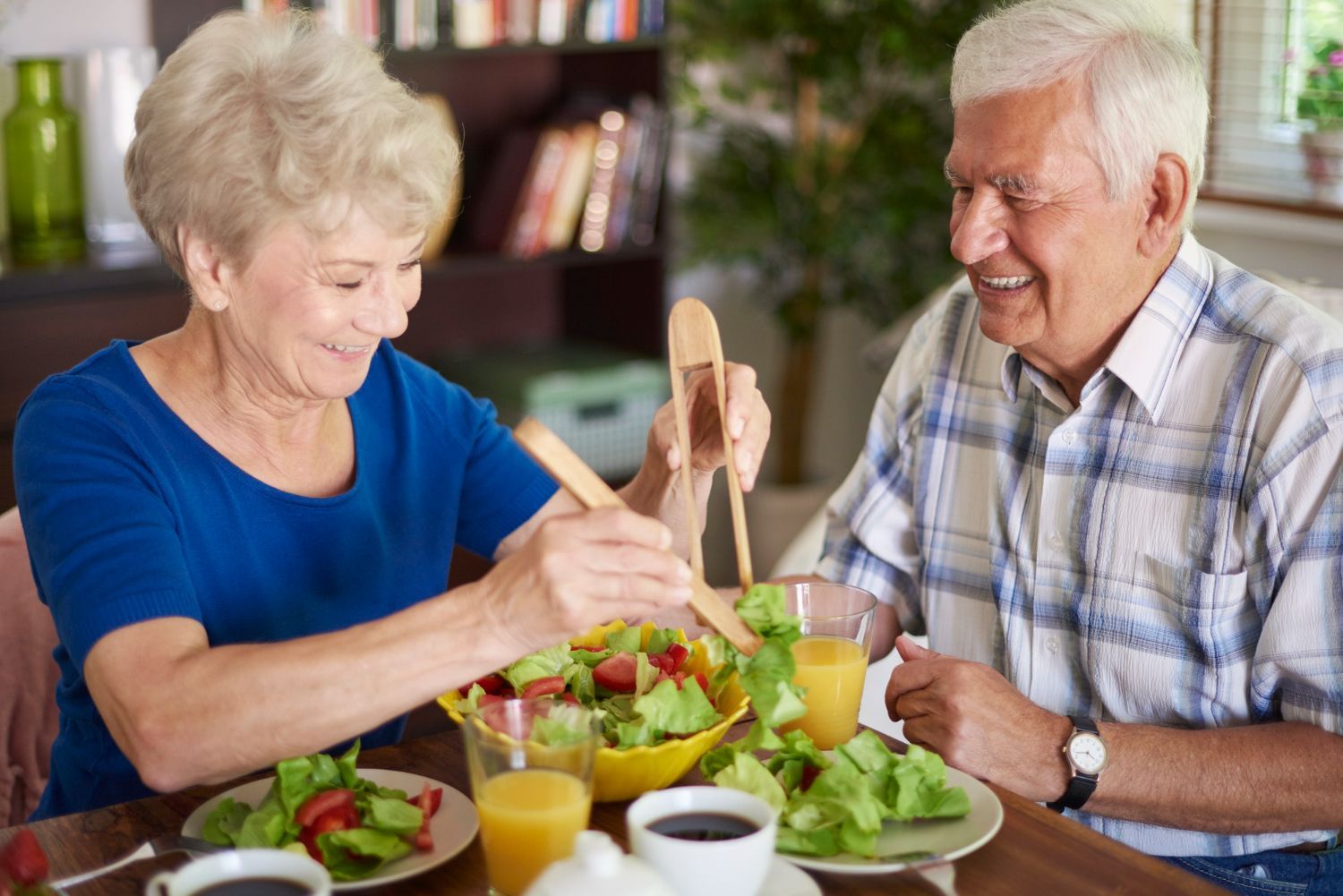 An elderly couple is sitting at a table eating a salad.