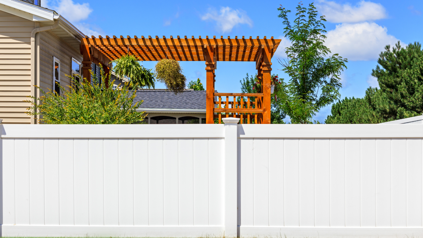 White vinyl fence with a wooden pergola in a backyard.
