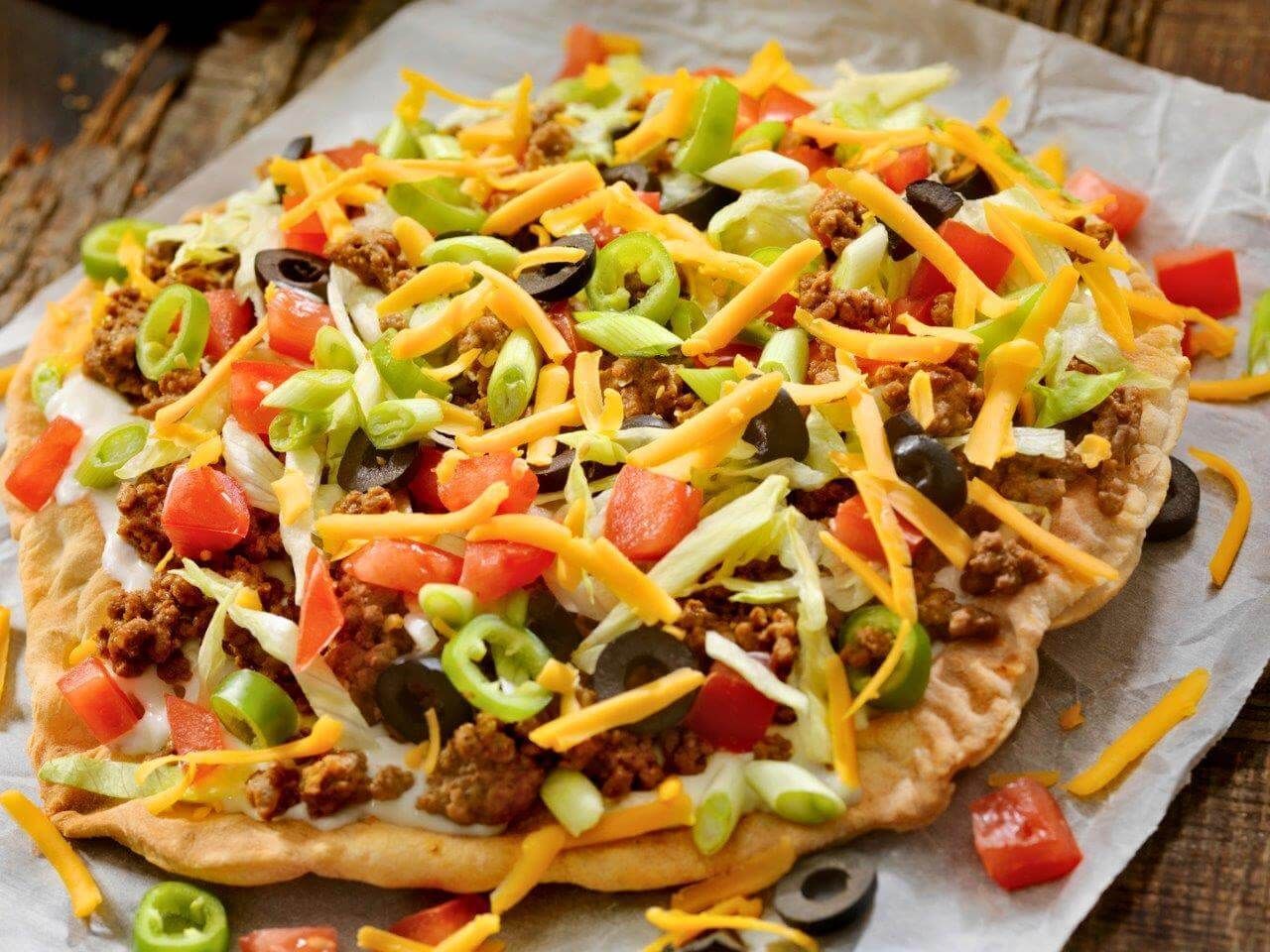 Una pizza taco è appoggiata su un pezzo di carta oleata su un tavolo di legno.