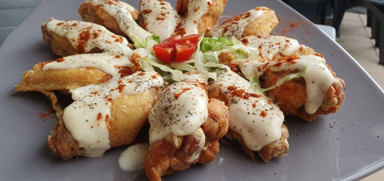 Un piatto di ali di pollo con salsa e pomodori su un tavolo.