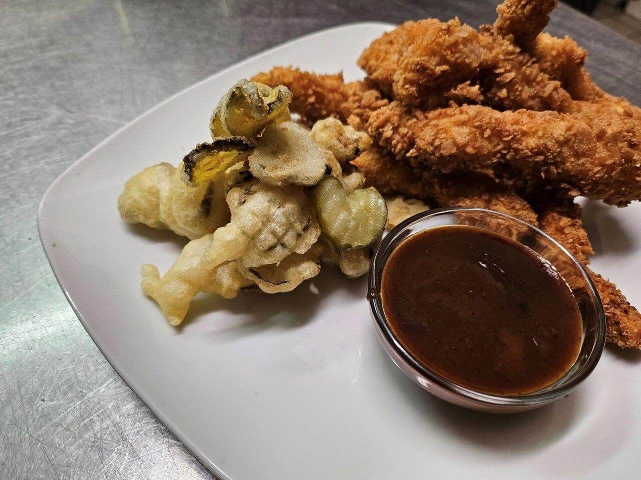 Un piatto bianco con sopra pollo fritto e verdure con salsa.