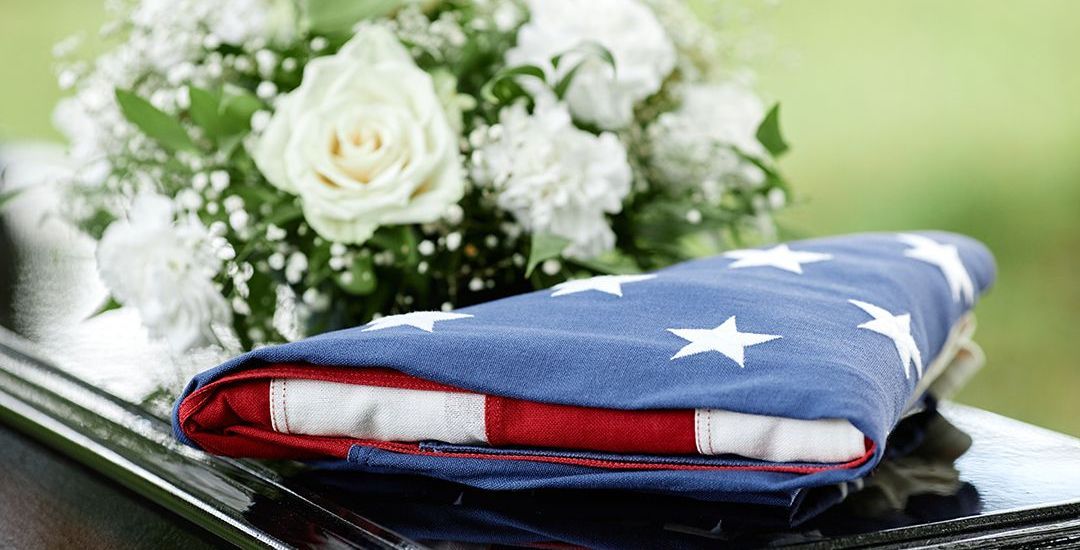 a folded american flag sits on a coffin next to a bouquet of white flowers